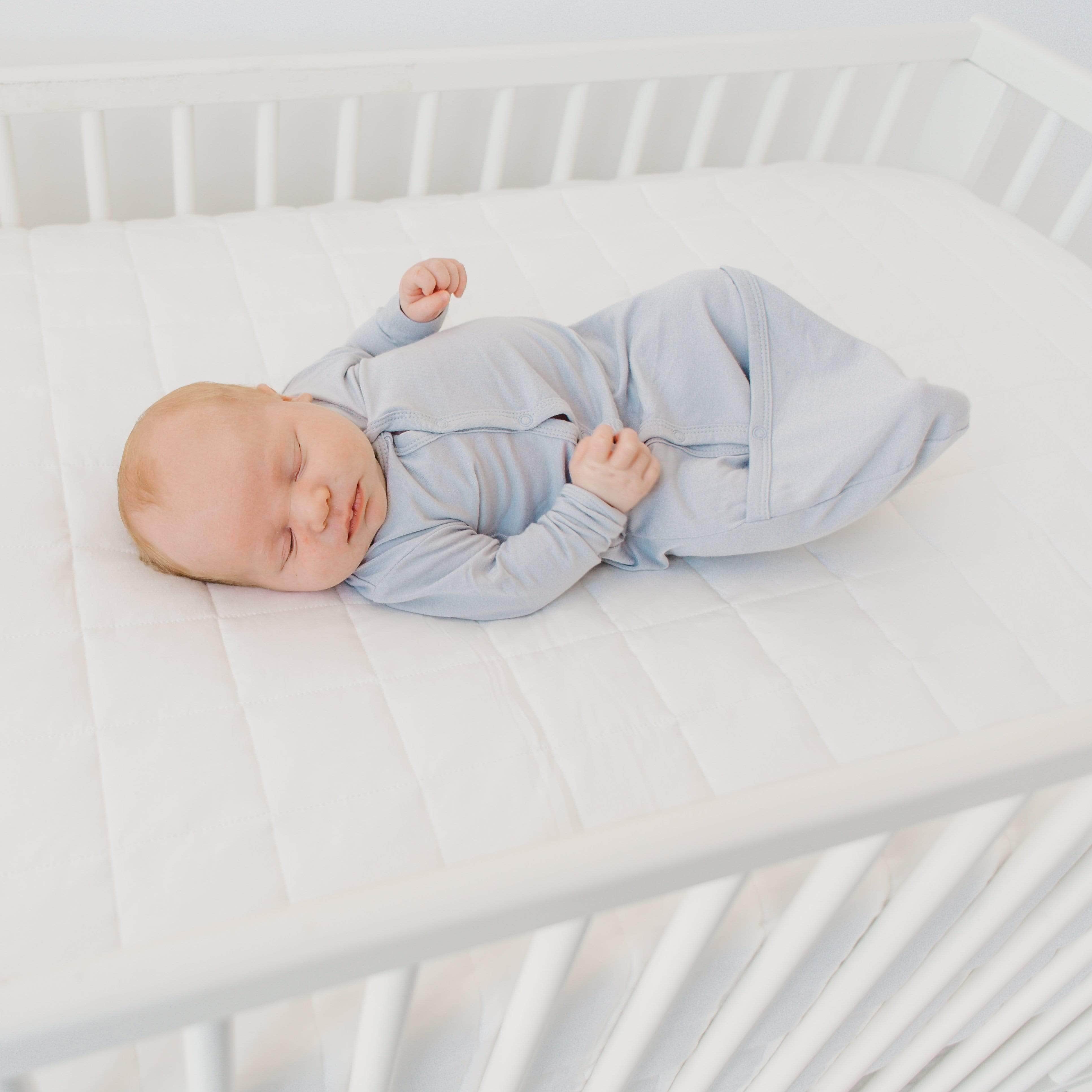 Newborn sleeping in blue swaddler pajamas