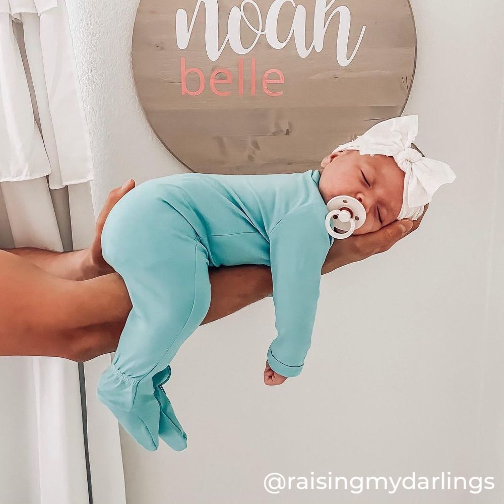 newborn baby wearing kyte baby jade footie and laying face down on someone's arm