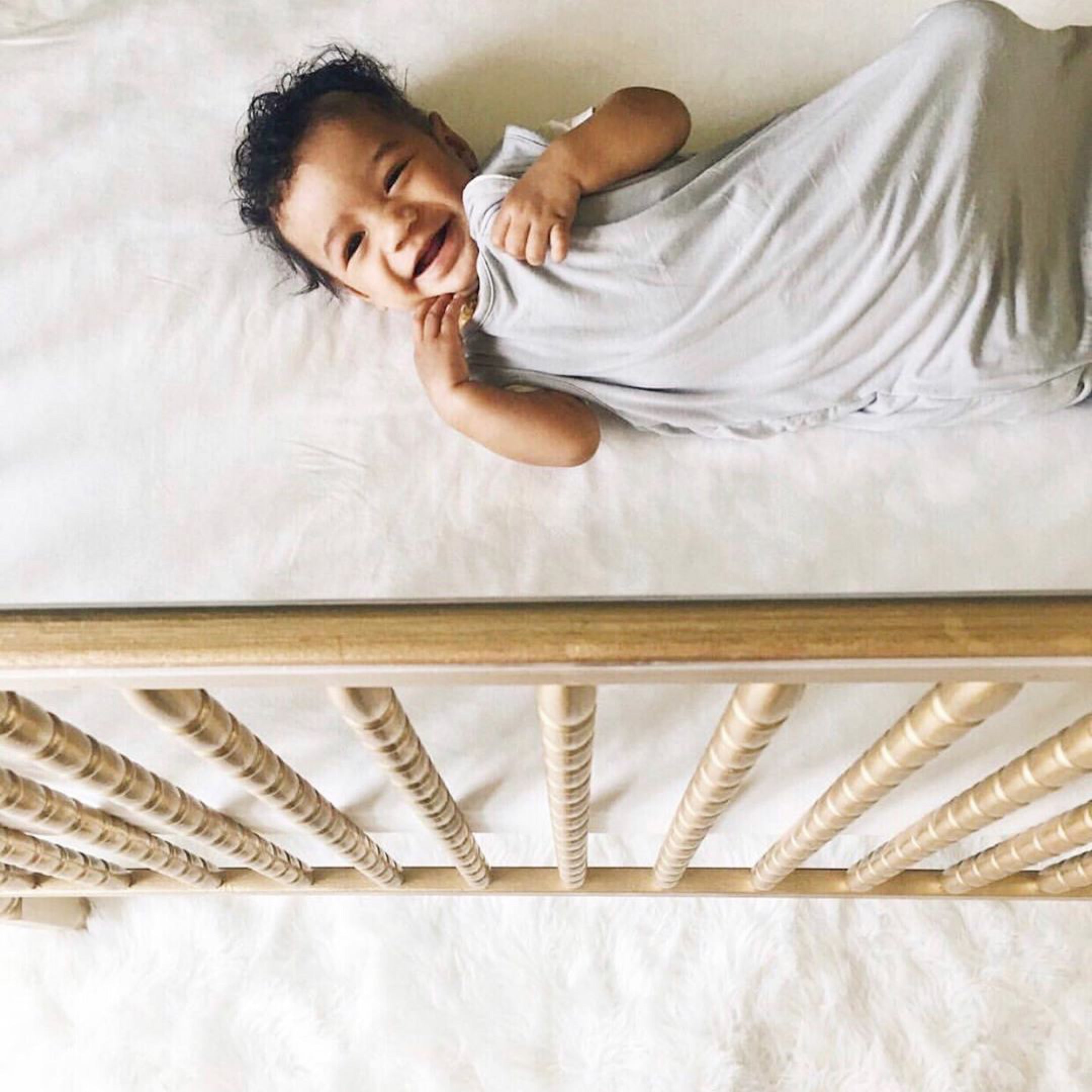 baby laughing and wearing a kyte baby sleep bag while laying in a crib
