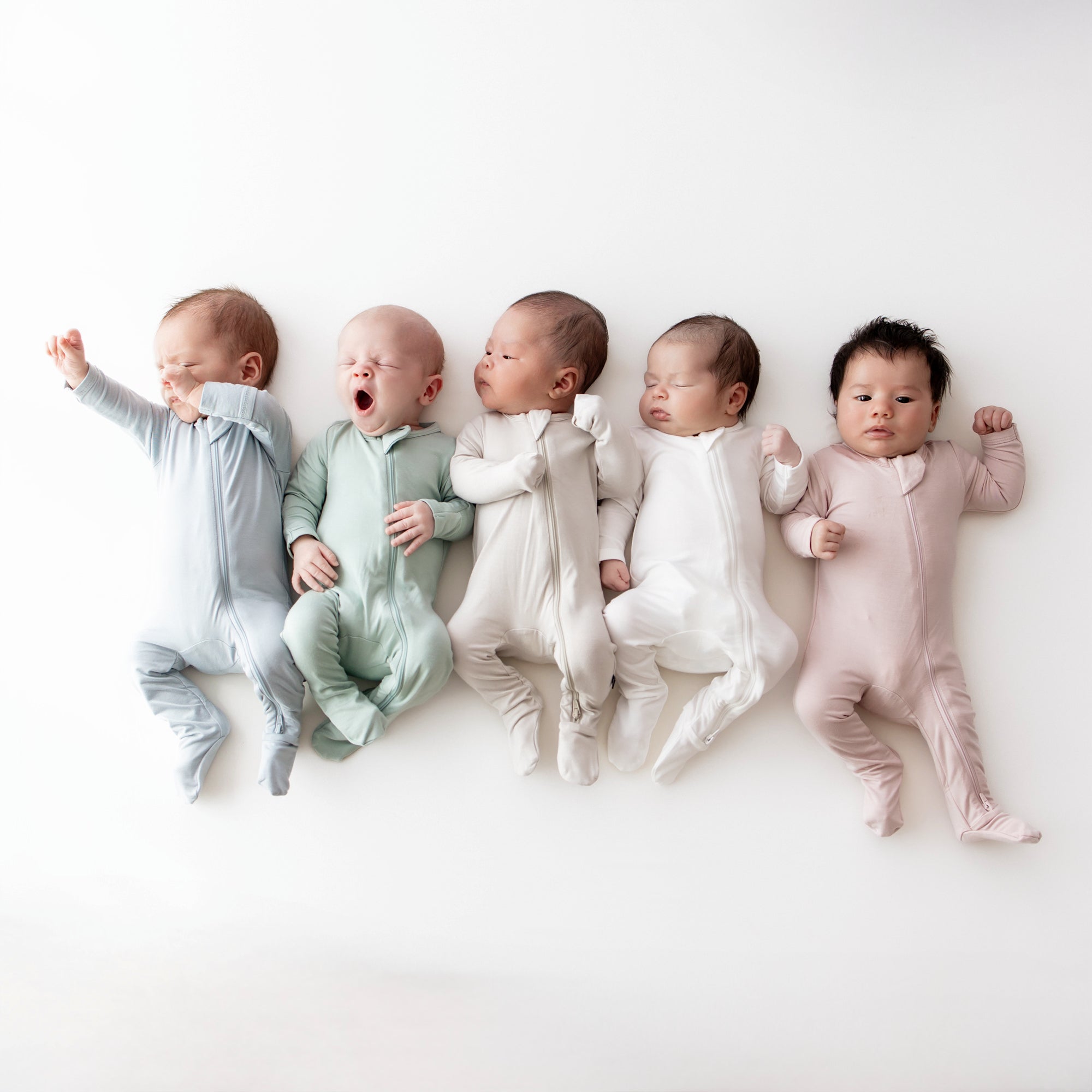 Newborns sleeping in zipper footie pajamas in pastel colors