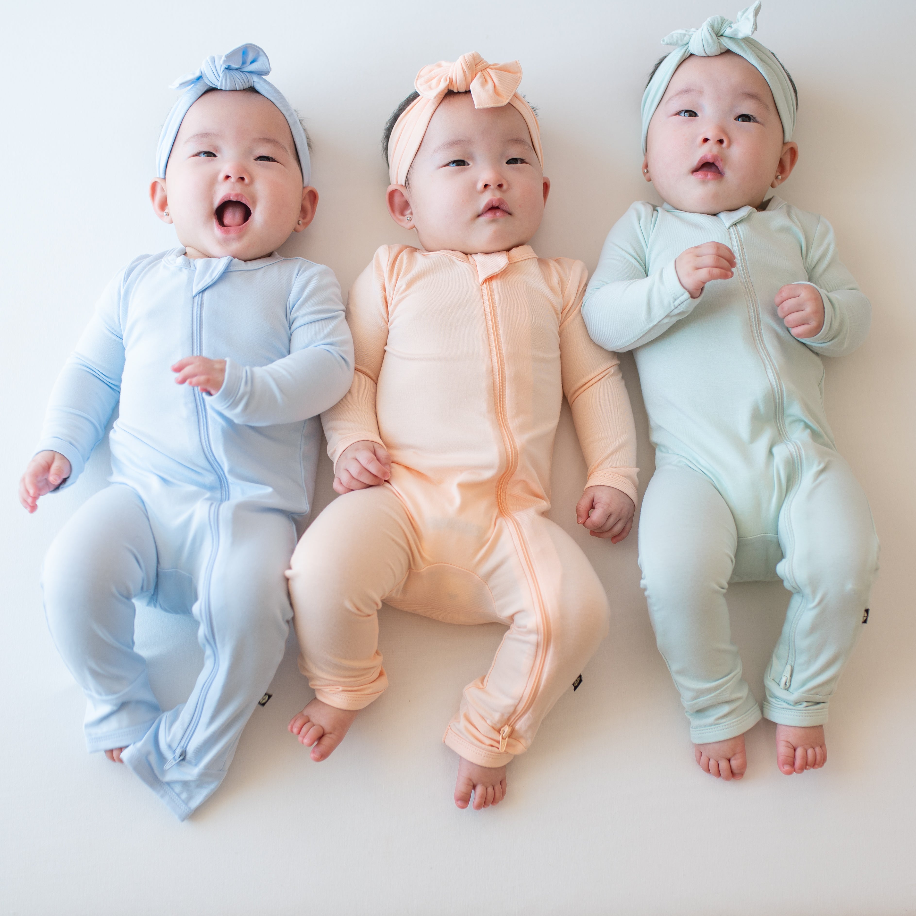 Three babies laying in zippered rompers