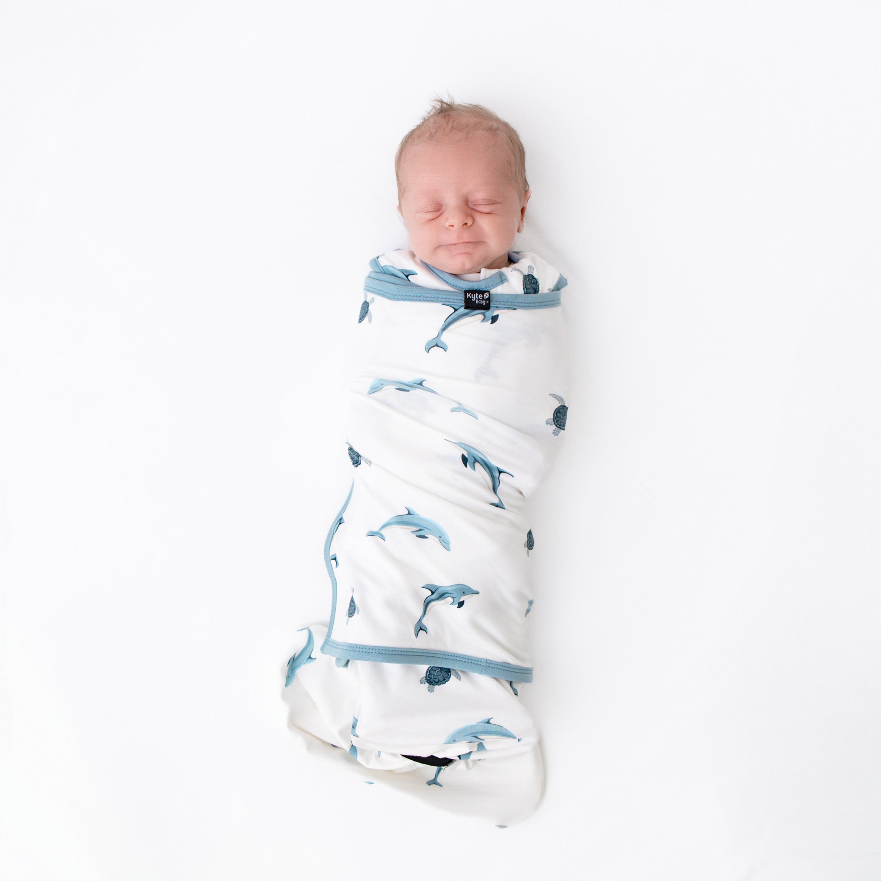 Sleeping baby swaddled in kyte sleep bag swaddler in dolphin 0.5 tog