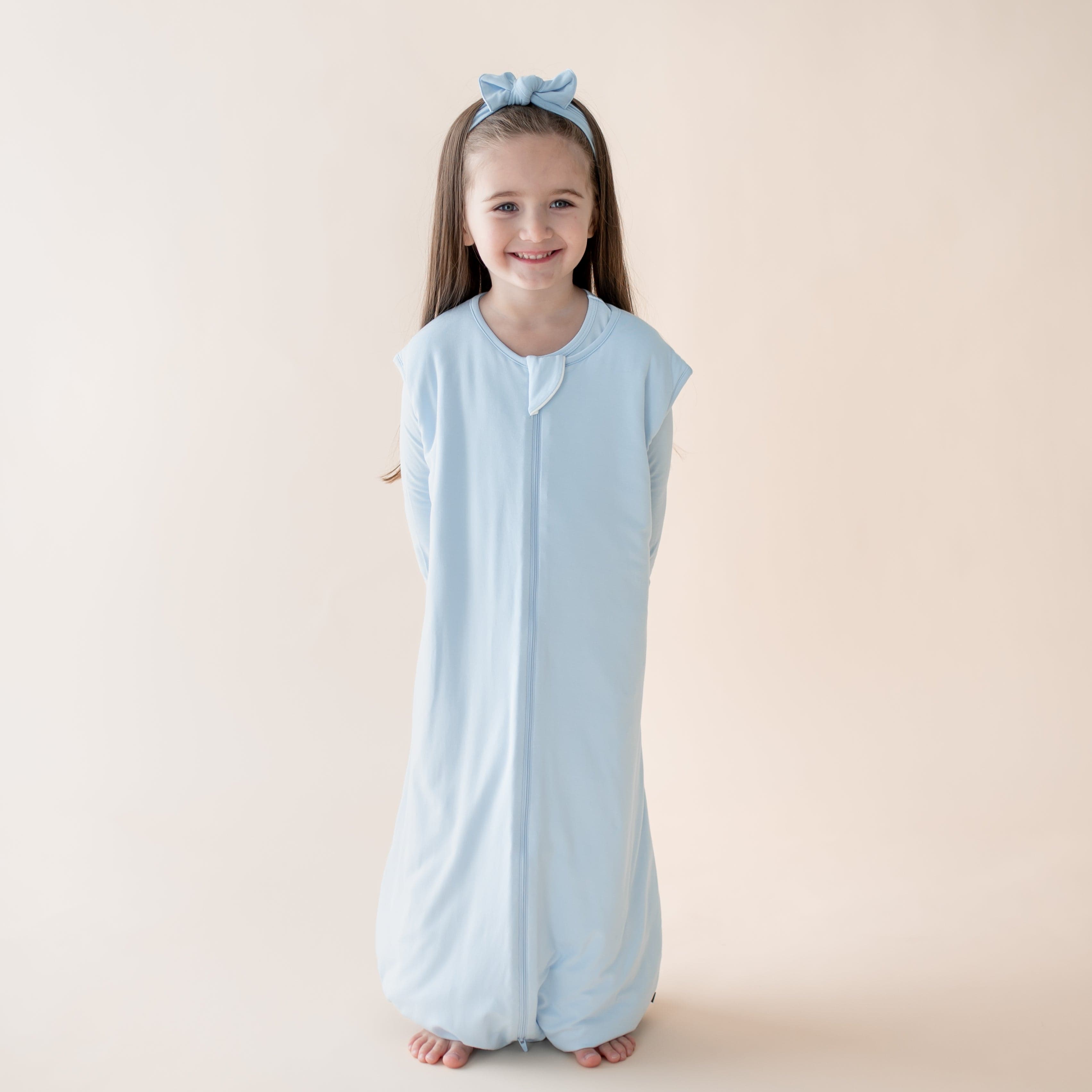 Young girl wearing a light blue sleeveless sleep bag walker with a zipper on a beige background