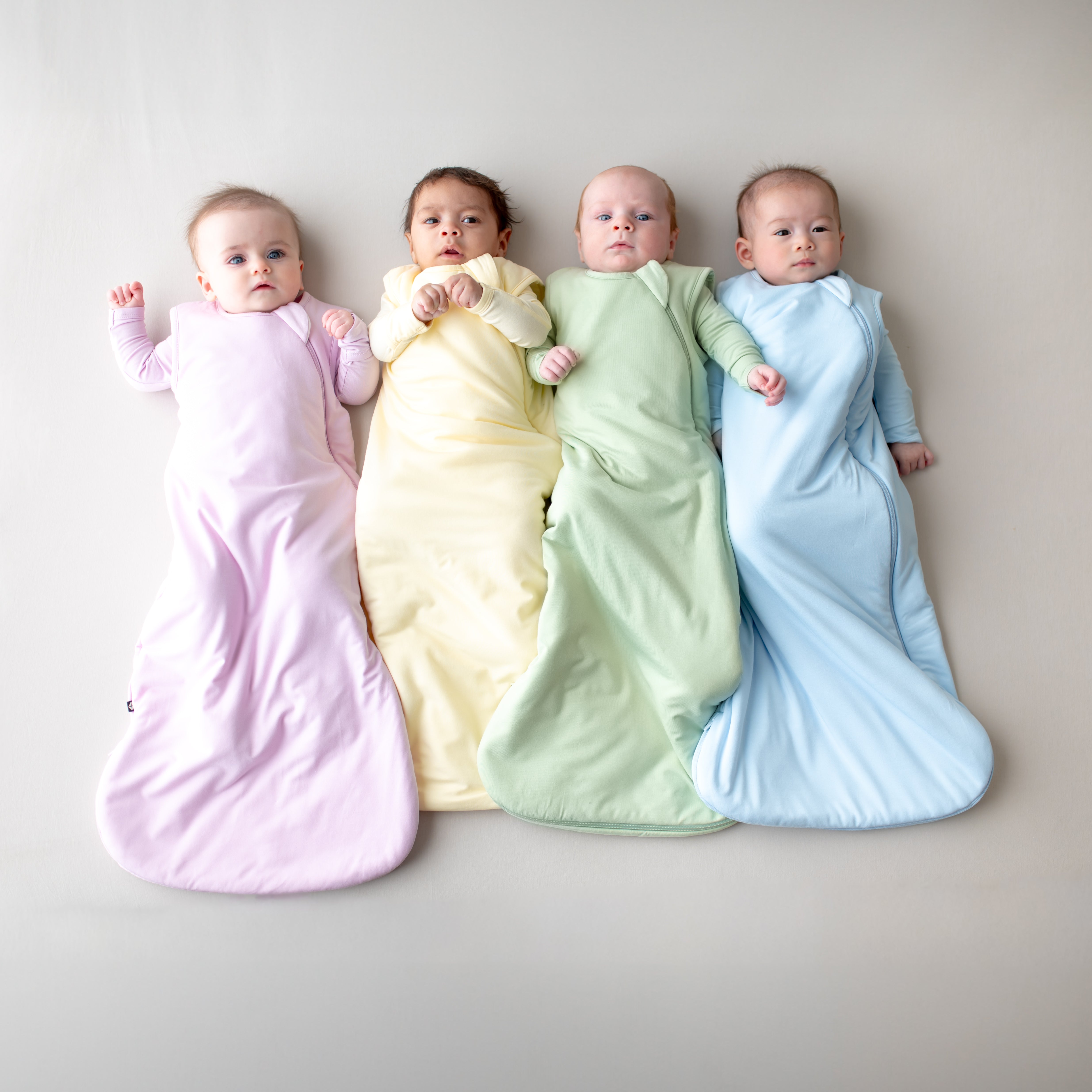 Four babies laying side by side wearing the 1.0 TOG Sleep bags in spring colors