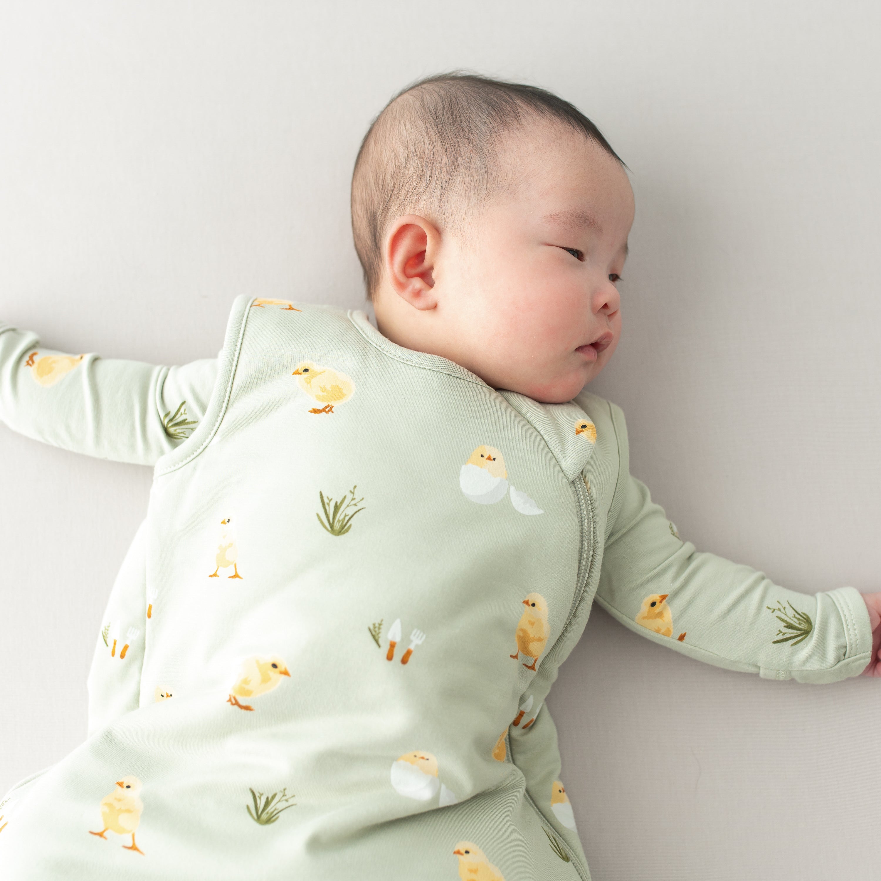 Baby wearing Sleep Bag in Aloe Chick 1.0 with matching PJs