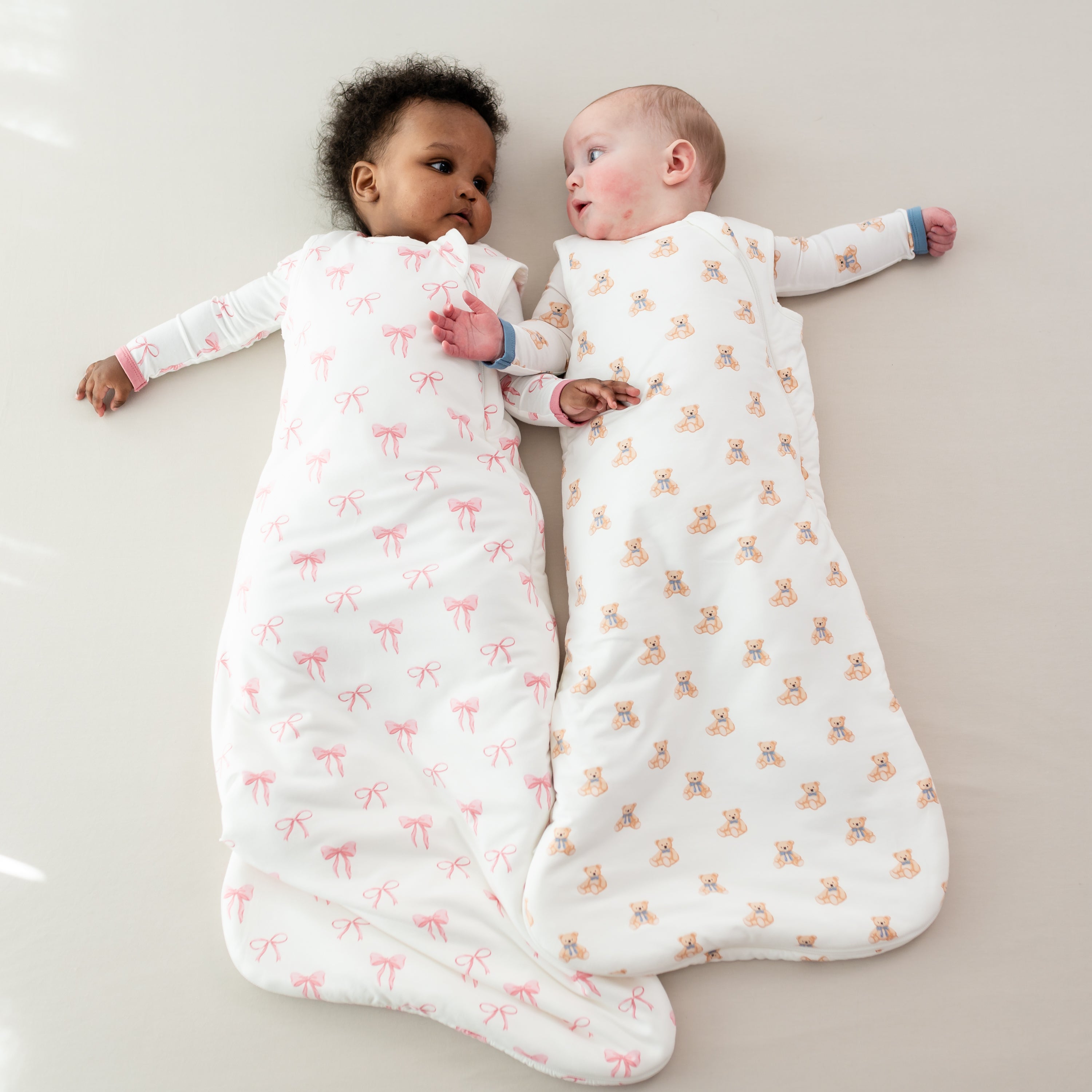 Two babies wearing TOG 1.0 Sleep Bags in Bow and Teddy Bear