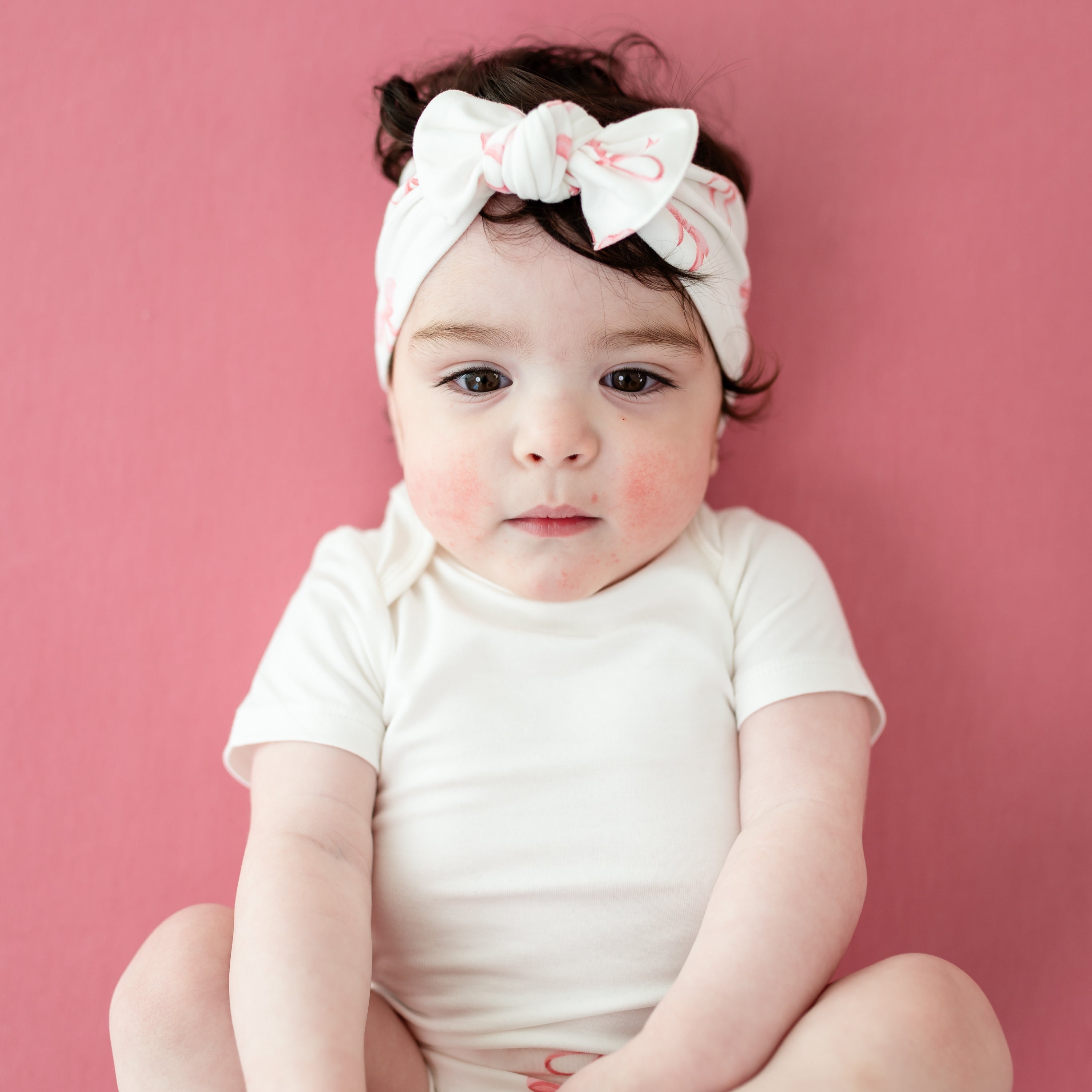 Baby wearing white onesie and knotted bow headband in pink bow print
