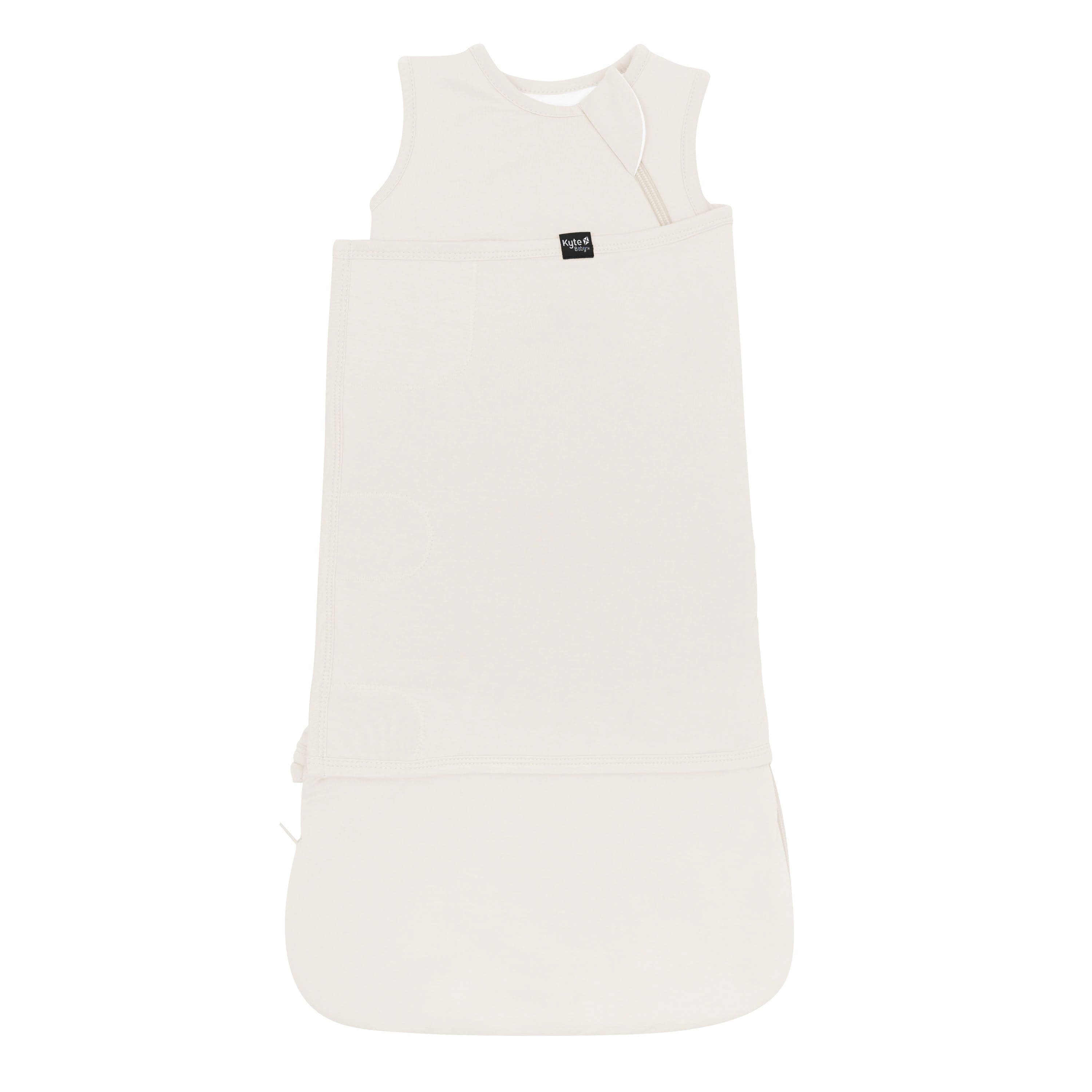 Sleep Bag Swaddler in Oat 1.0 shown swaddled with the Black Kyte Baby tag visible