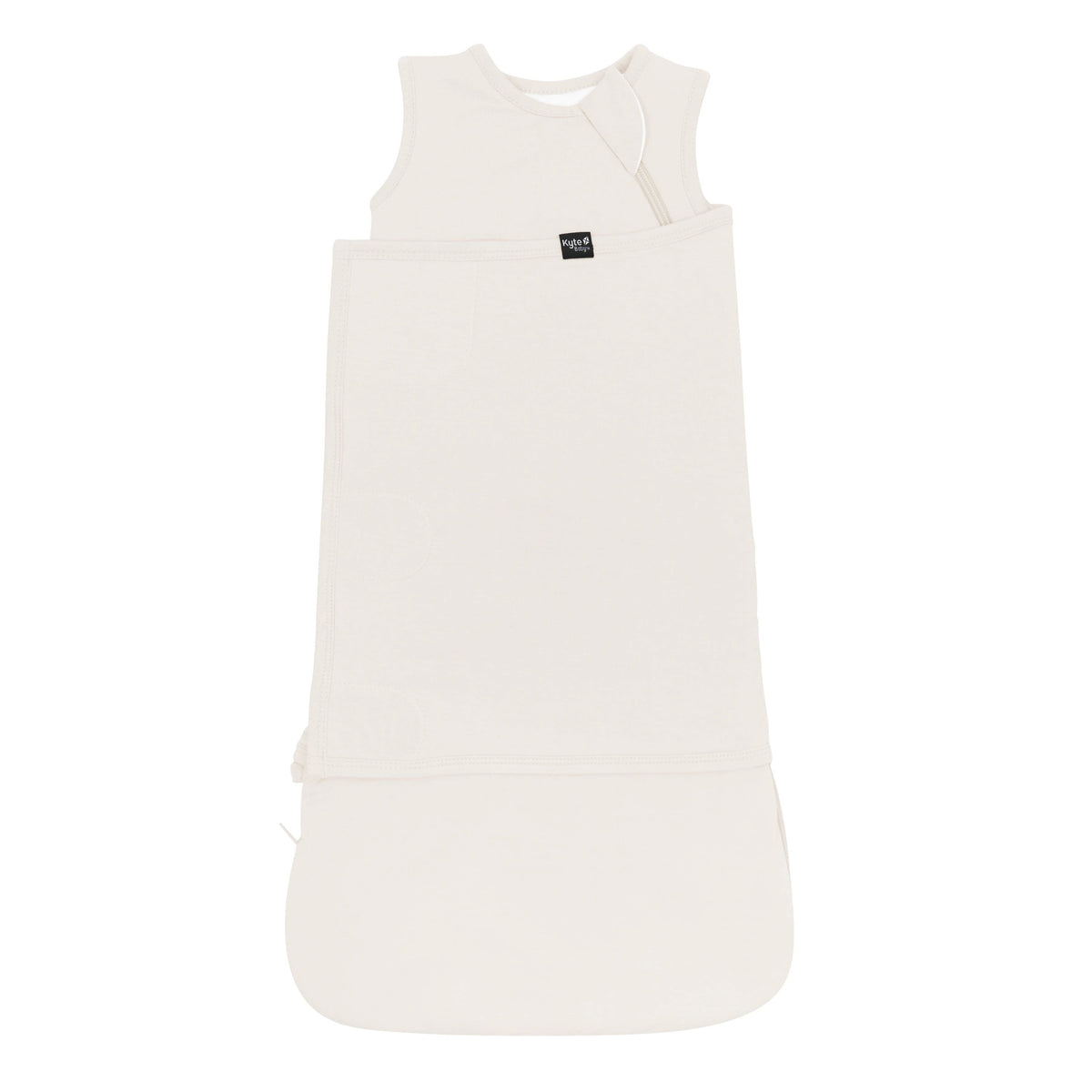 Sleep Bag Swaddler in Oat 1.0 shown swaddled with the Black Kyte Baby tag visible