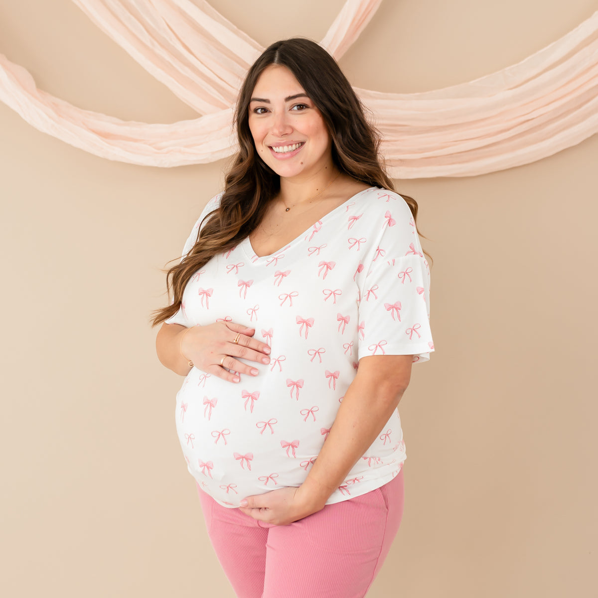 Pregnant woman modeling Women’s Relaxed Fit V-Neck in Bow with Apple Blossom Ribbed Jogger Pants. Hands holding baby bump