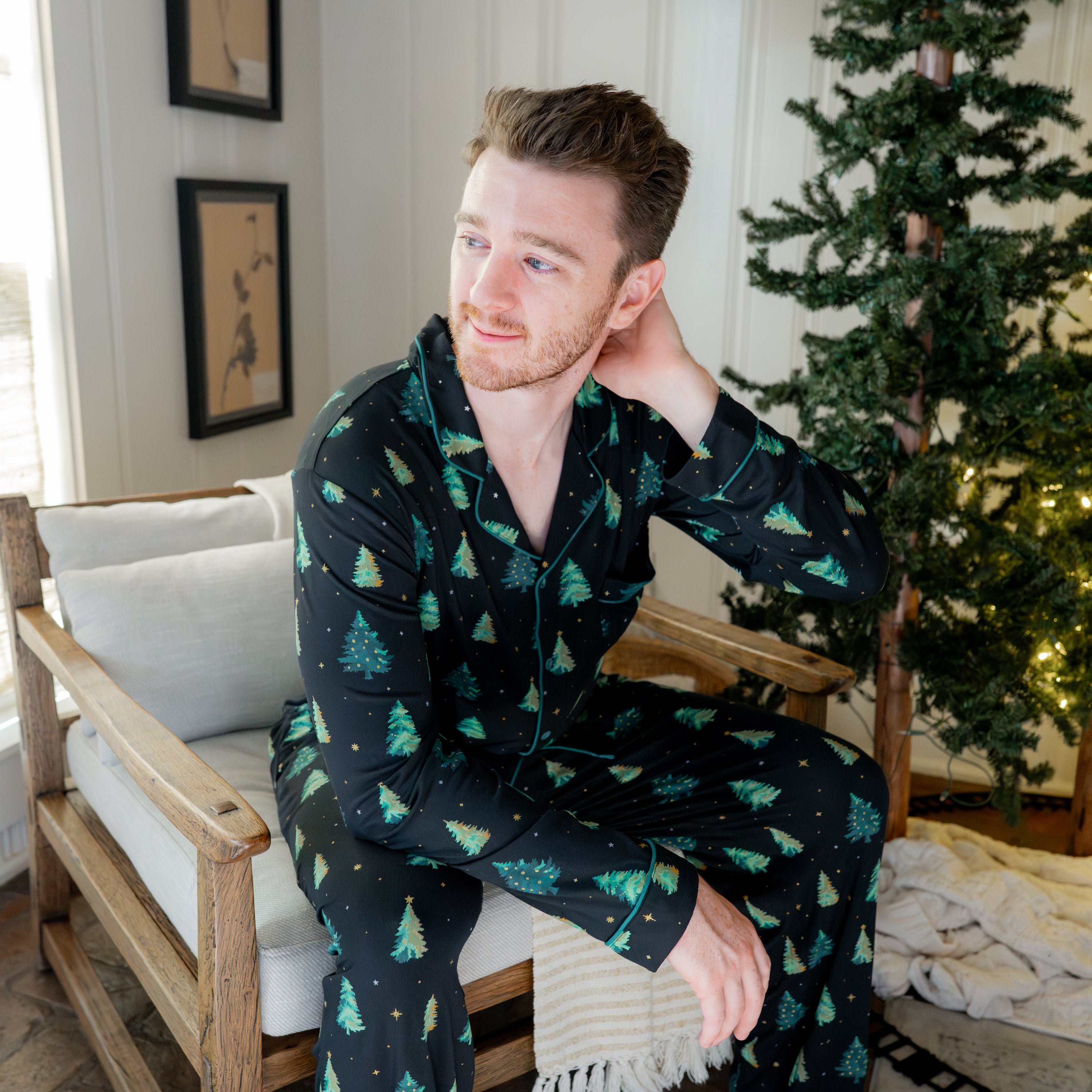 Male model sitting on a chair wearing the Men's Long Sleeve Pajama Set in Twinkle Tree