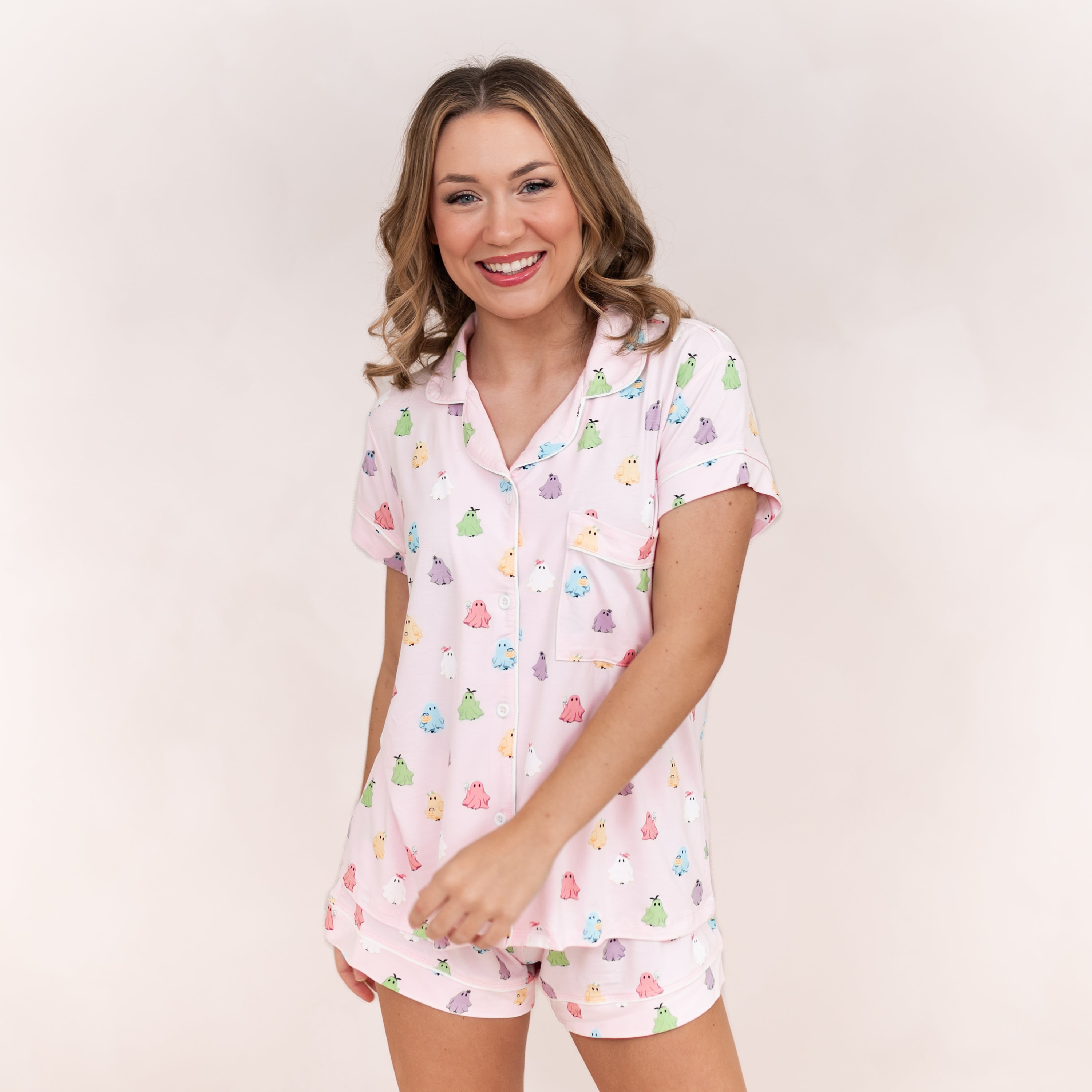 Smiling model swinging her arm wearing the Women's Short Sleeve Pajama Set in Pastel Ghost in front of a light beige background