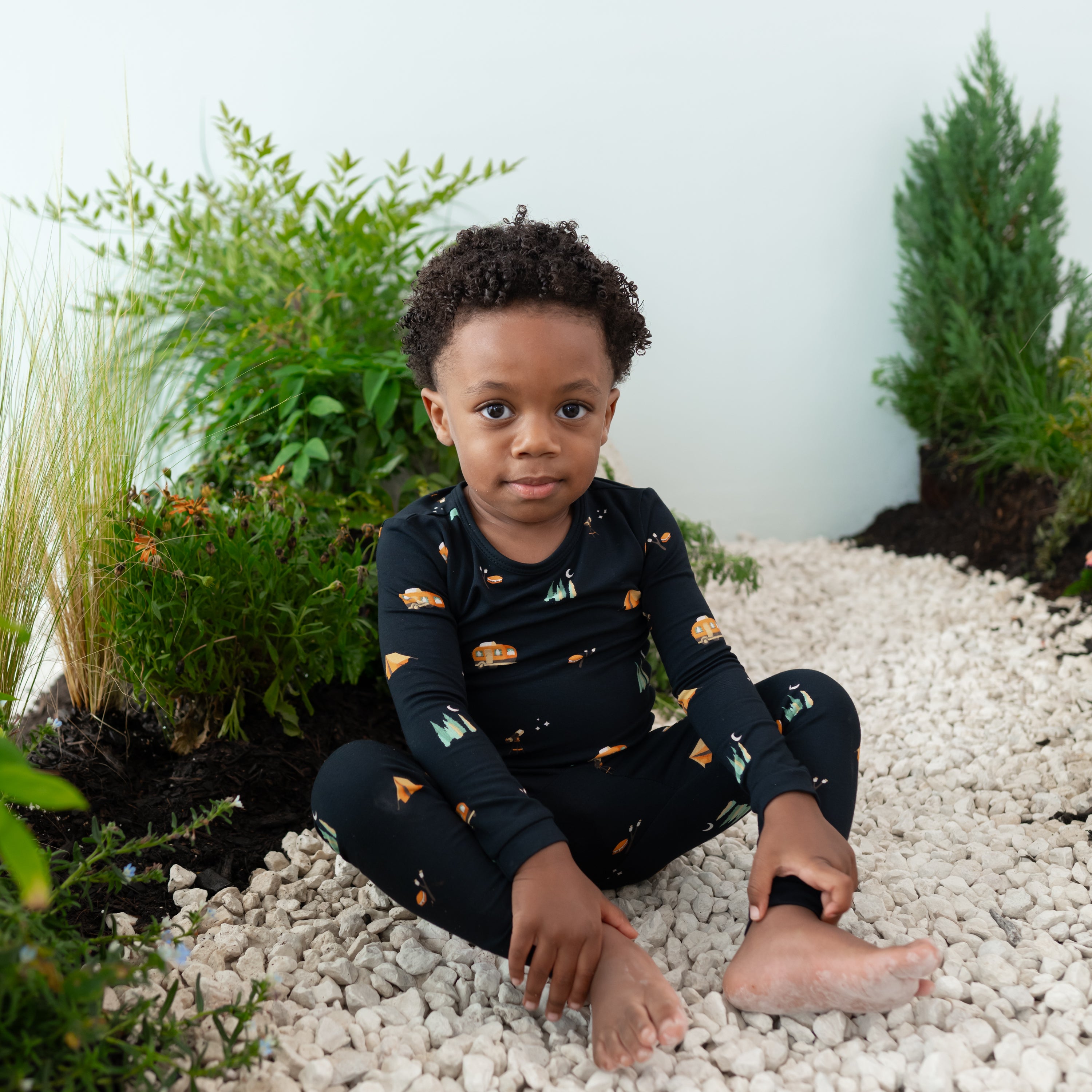Young boy model wearing the Long Sleeve Pajamas in Under the Stars sitting on rocks in an outdoor scene back drop