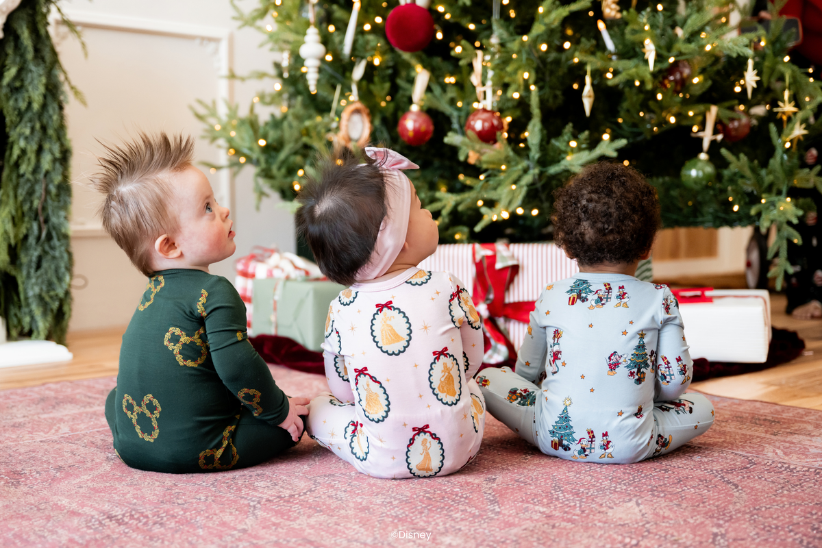 3 babies sitting wearing Kyte x Disney collection rompers in front of a christmas tree