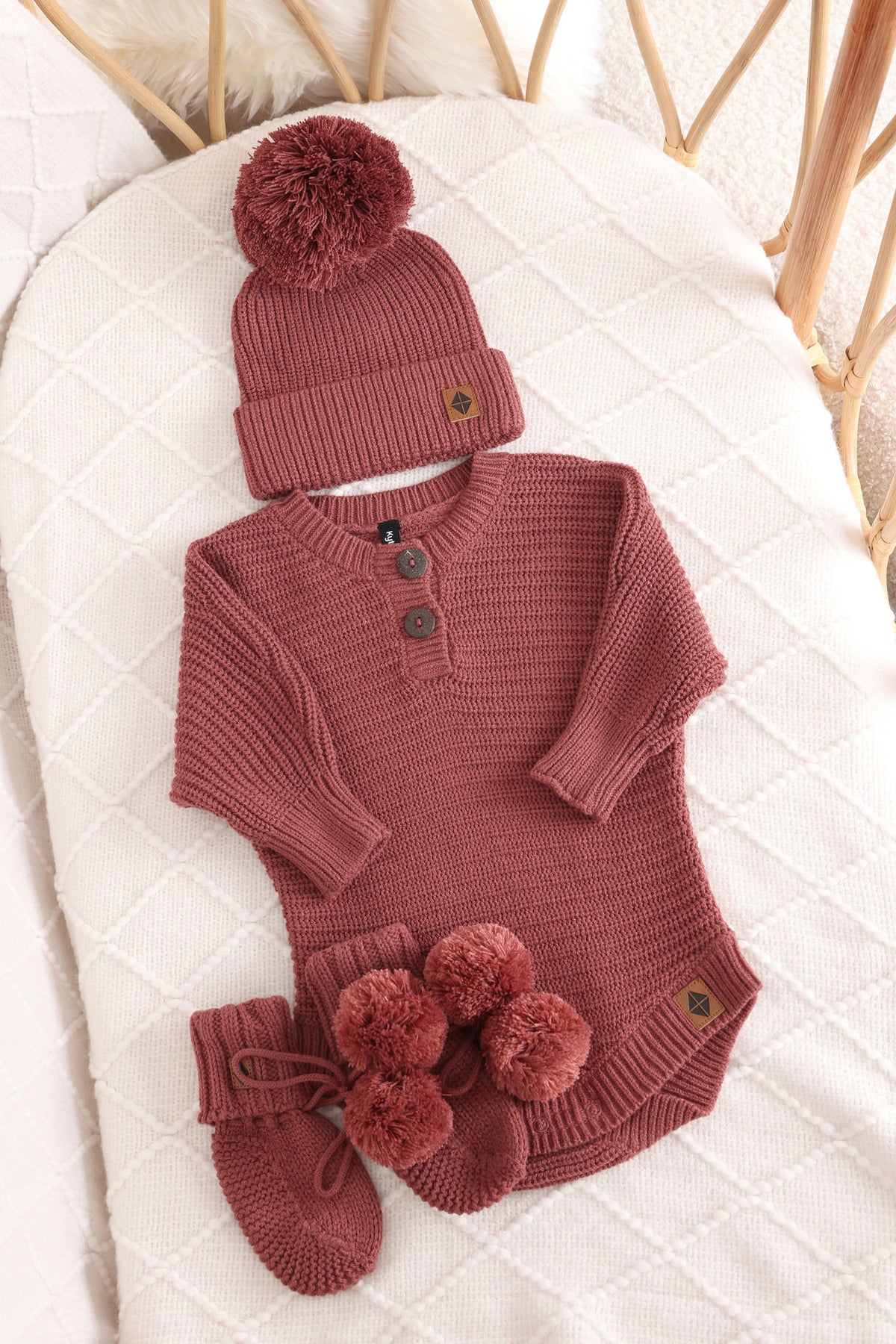 Chunky knit pom beanie, chunky knit romper and knit booties in ember laid in a crib