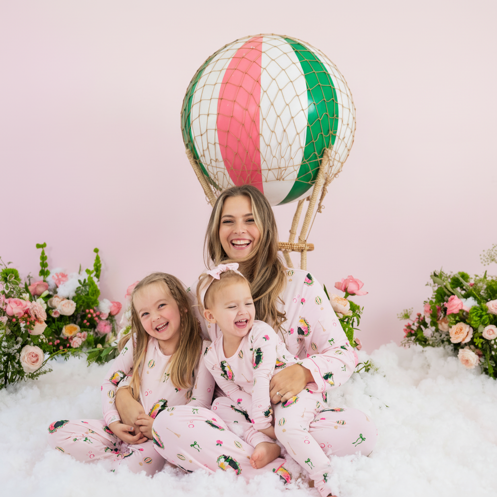 Mother and two daughters sitting in front of a prop hot air balloon matching in soft and breathable Kyte Baby pajamas in the Wicked print