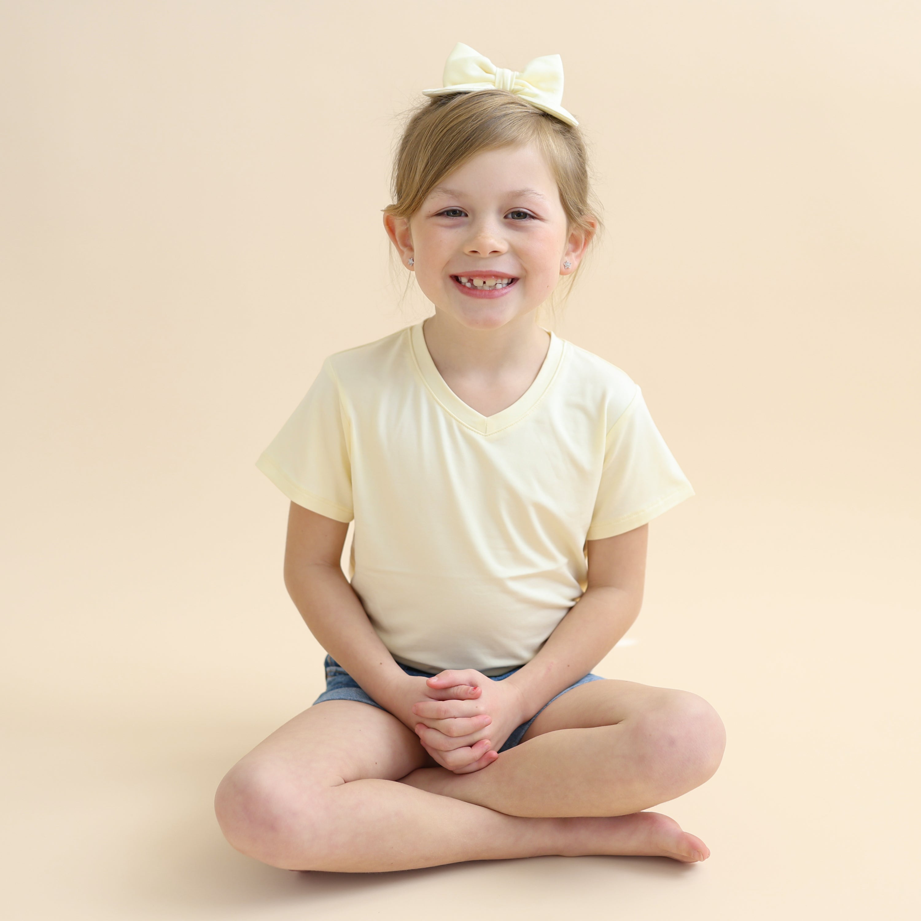 Young smiling girl sitting cross legged on the floor wearing the Medium Alligator Clip Bow in Chamomile with a matching shirt