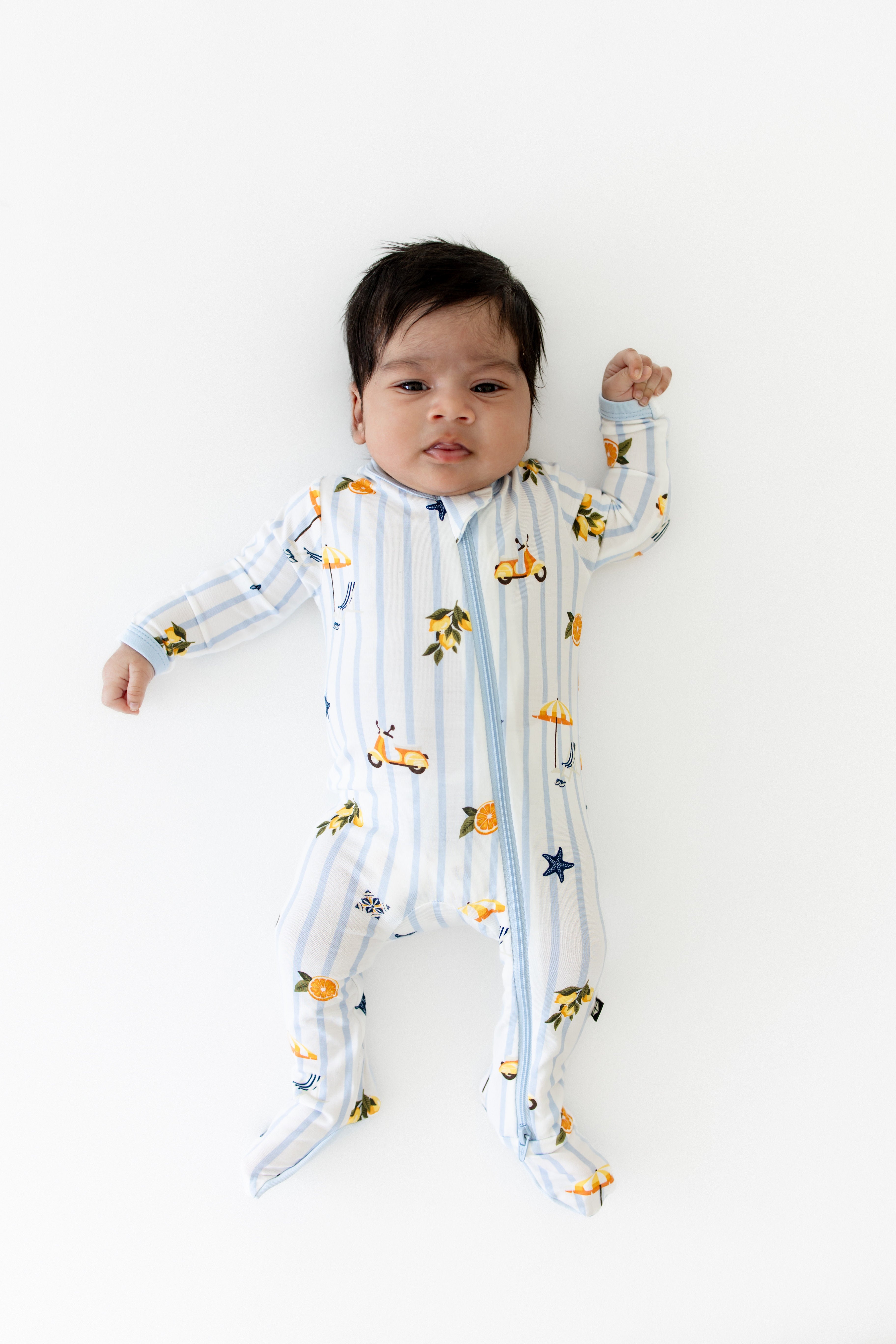 Newborn laying on a white surface wearing the Zippered Footie in Amalfi Coast