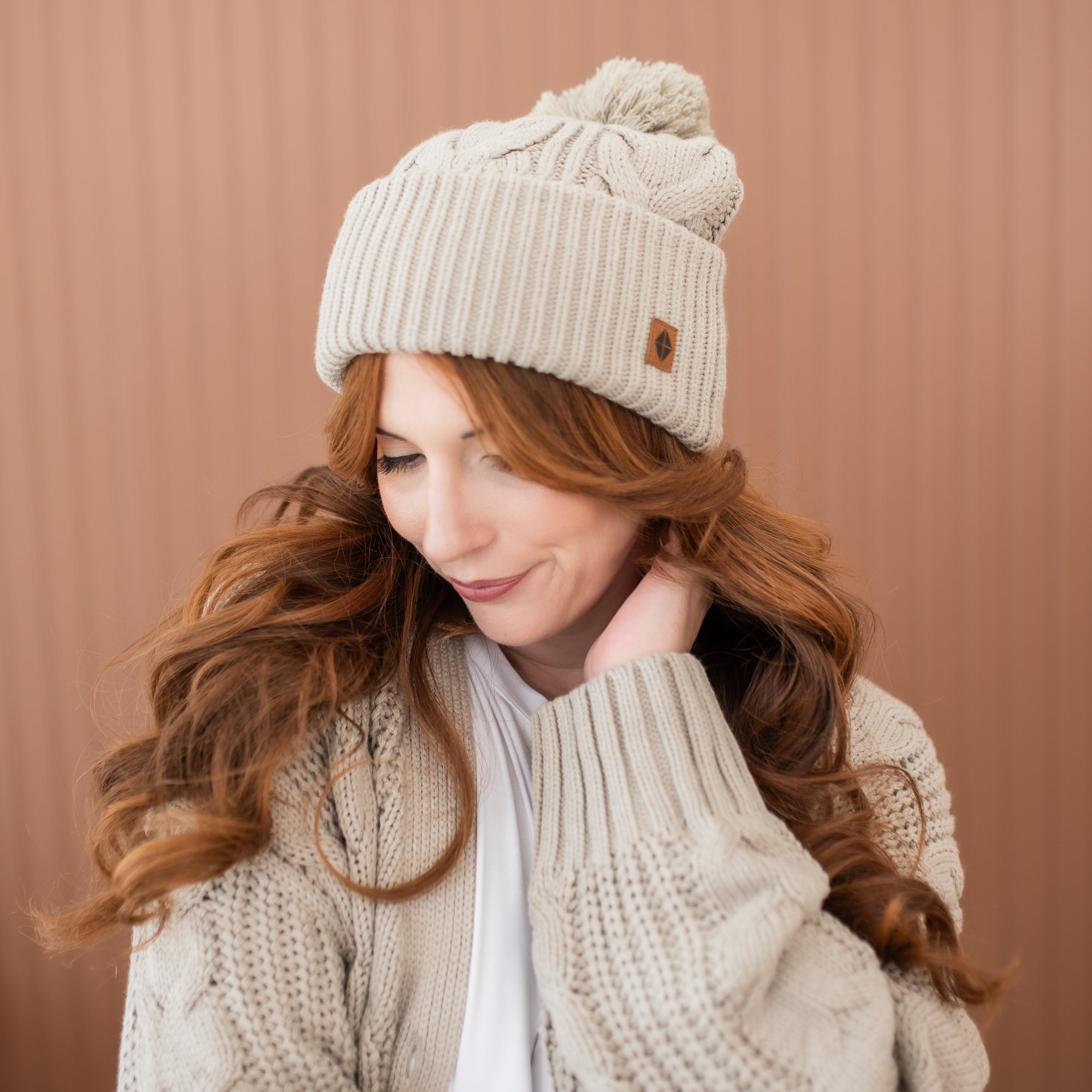 Female model wearing the Cable Knit Adult Pom Beanie in Almond paired with the Cable Knit Almond Cardigan