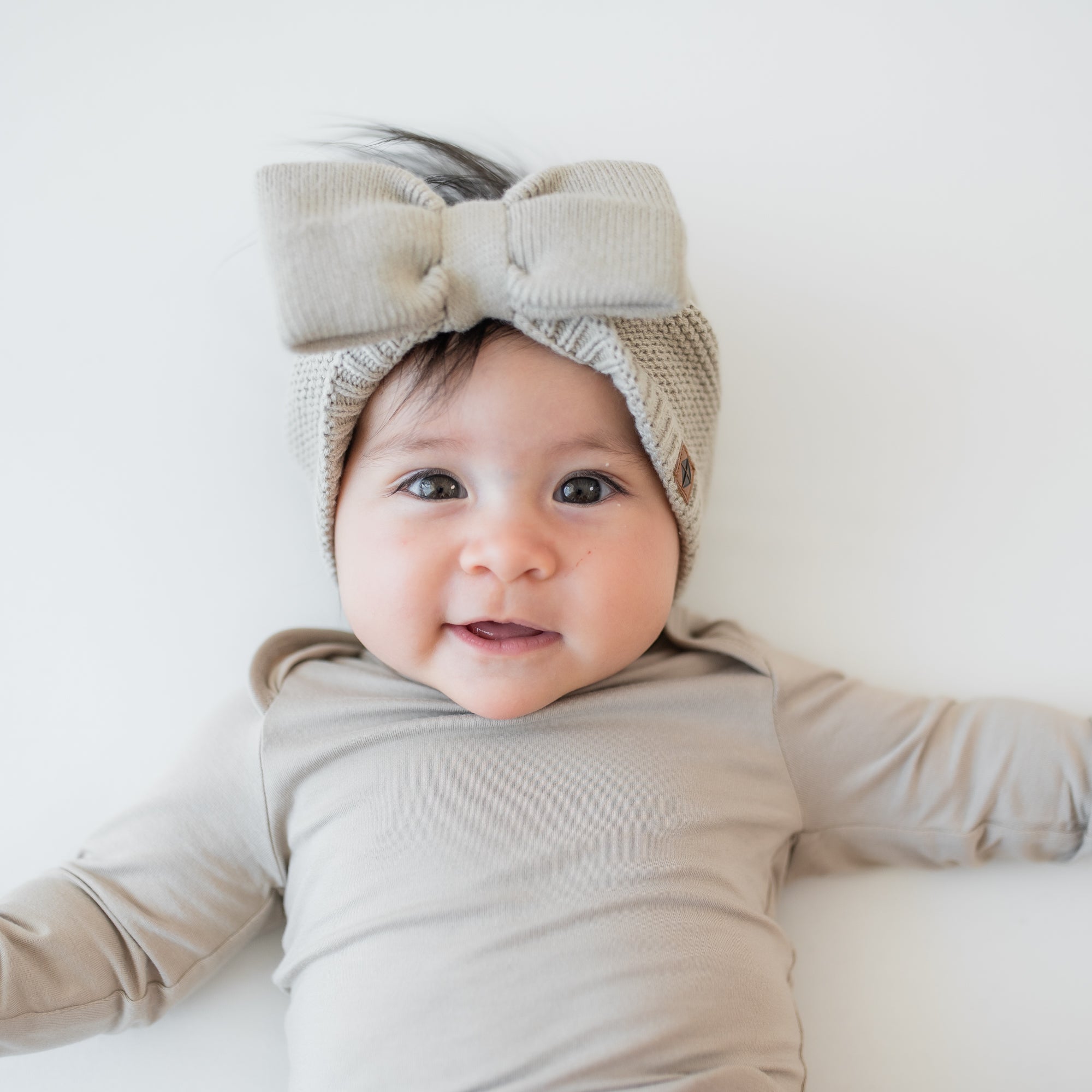 Infant laying down wearing the Chunky Knit Bow Headband in Almond paired with a matching long sleeve bodysuit