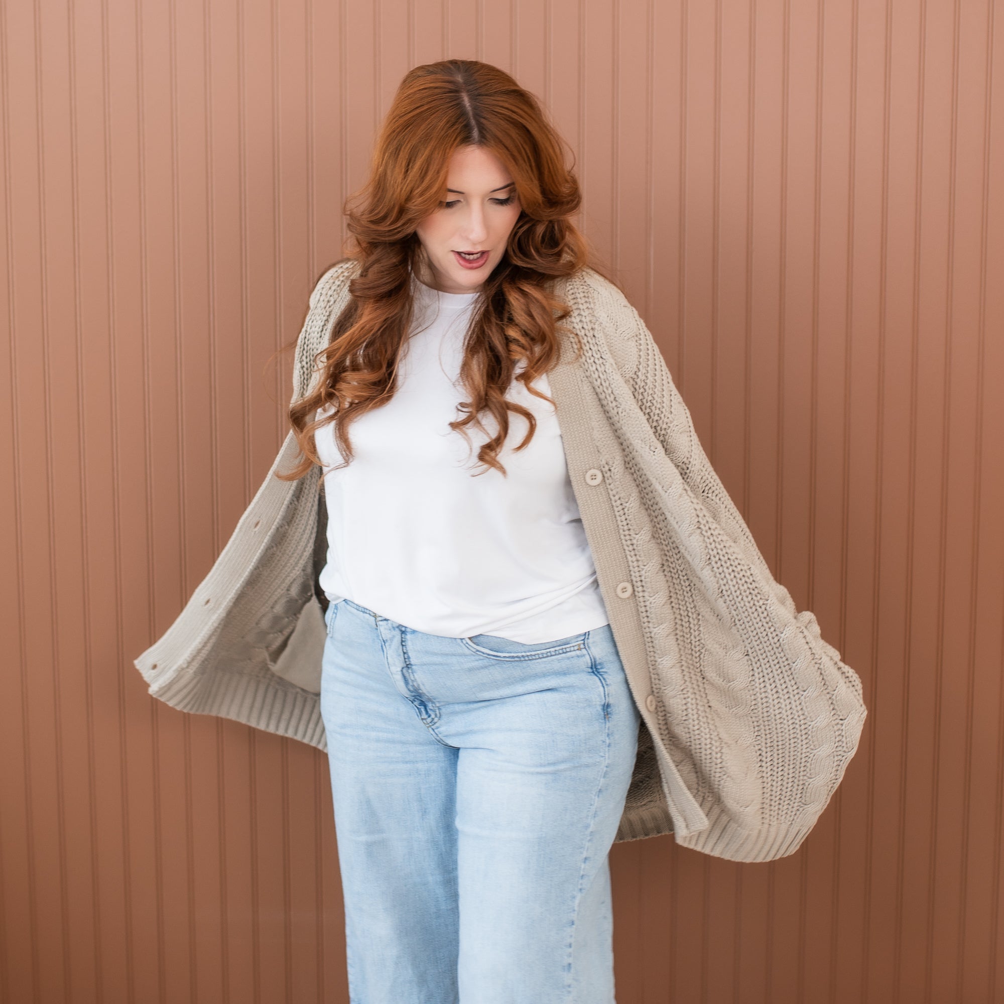 Female model standing with her hands in the pocket of the Cable Knit Adult Cardigan in Almond wearing a white shirt and light wash jeans