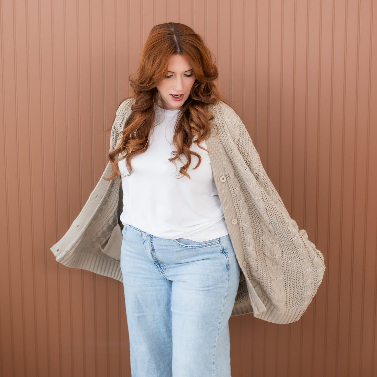 Female model standing with her hands in the pocket of the Cable Knit Adult Cardigan in Almond wearing a white shirt and light wash jeans
