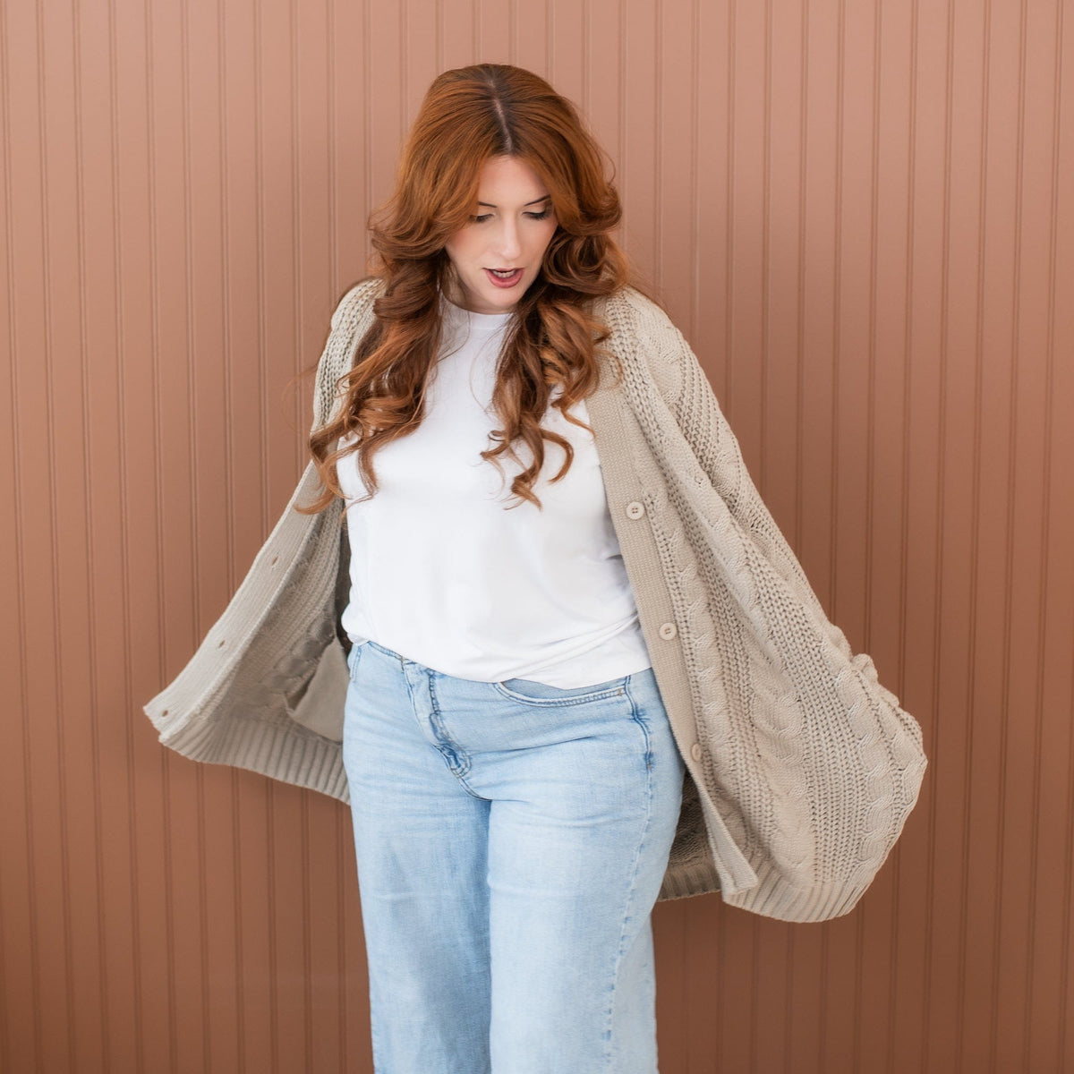 Female model standing with her hands in the pocket of the Cable Knit Adult Cardigan in Almond wearing a white shirt and light wash jeans