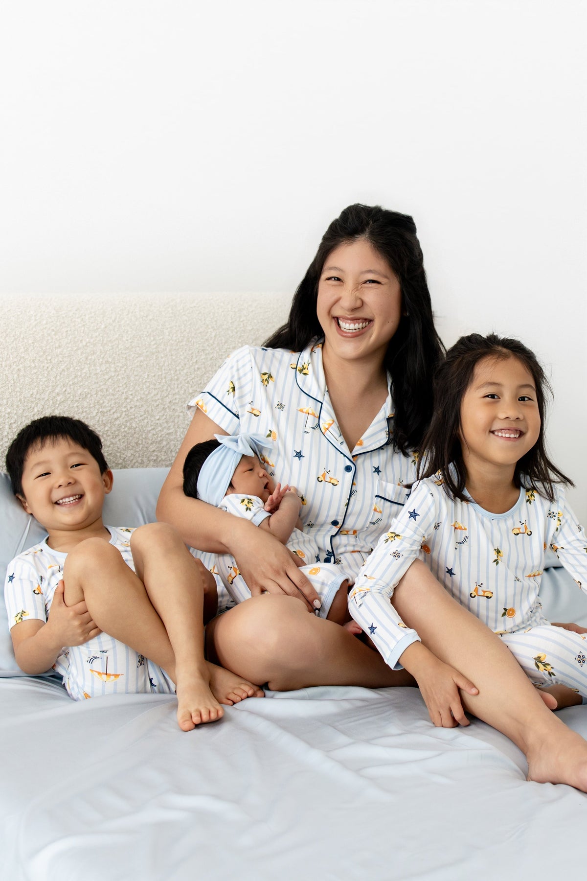 Family including a mom and 3 children wearing matching amalfi coast inspired pajamas on a bed with blue bedding
