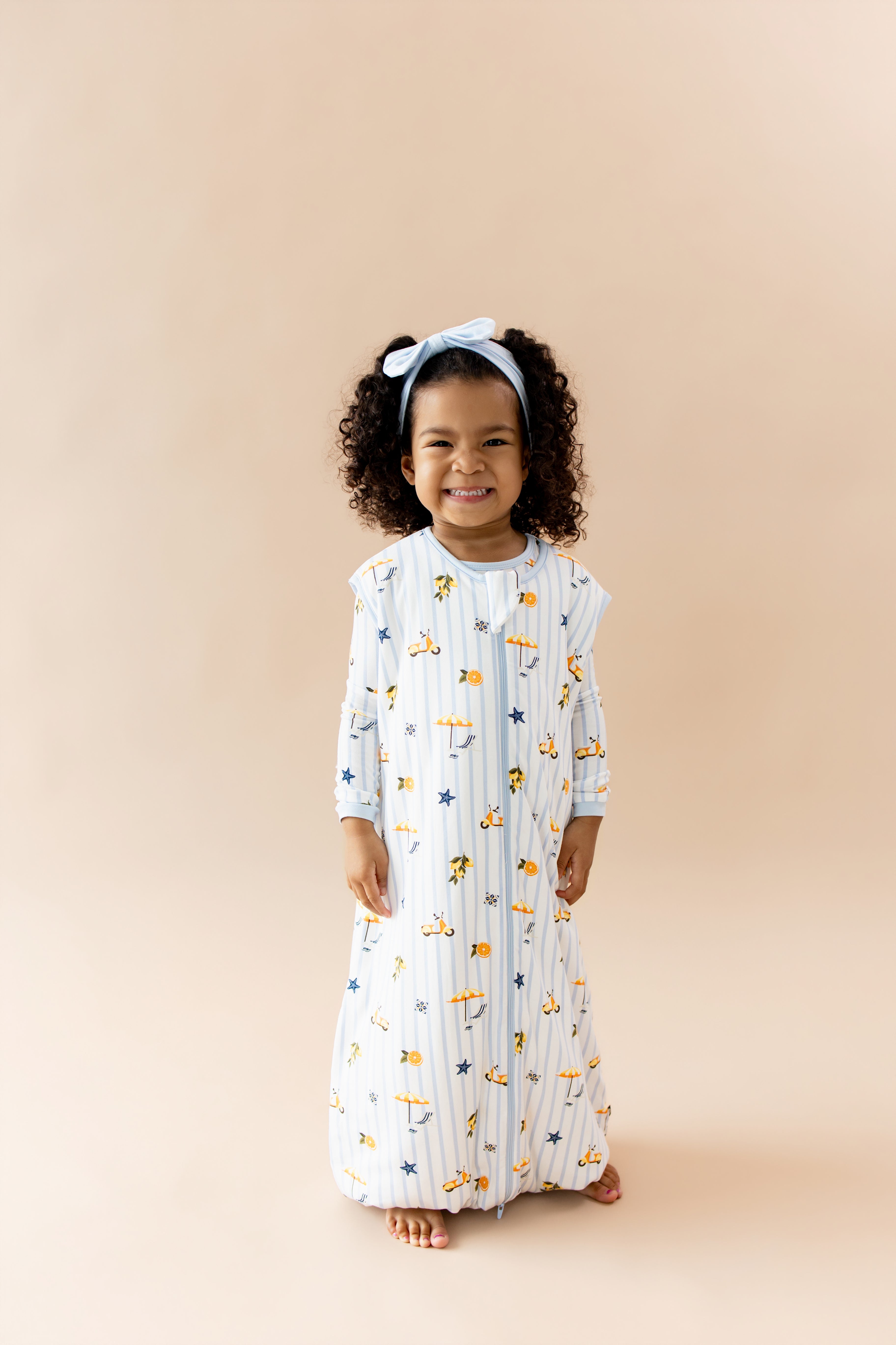 Smiling girl wearing the Sleep Bag Walker in Amalfi Coast 1.0 with light blue bow