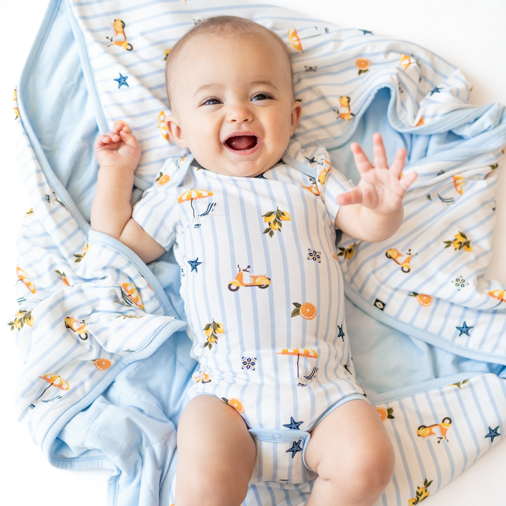 Newborn baby in a short sleeve bamboo bodysuit with an amalfi coast inspired pattern laying on a matching baby blanket