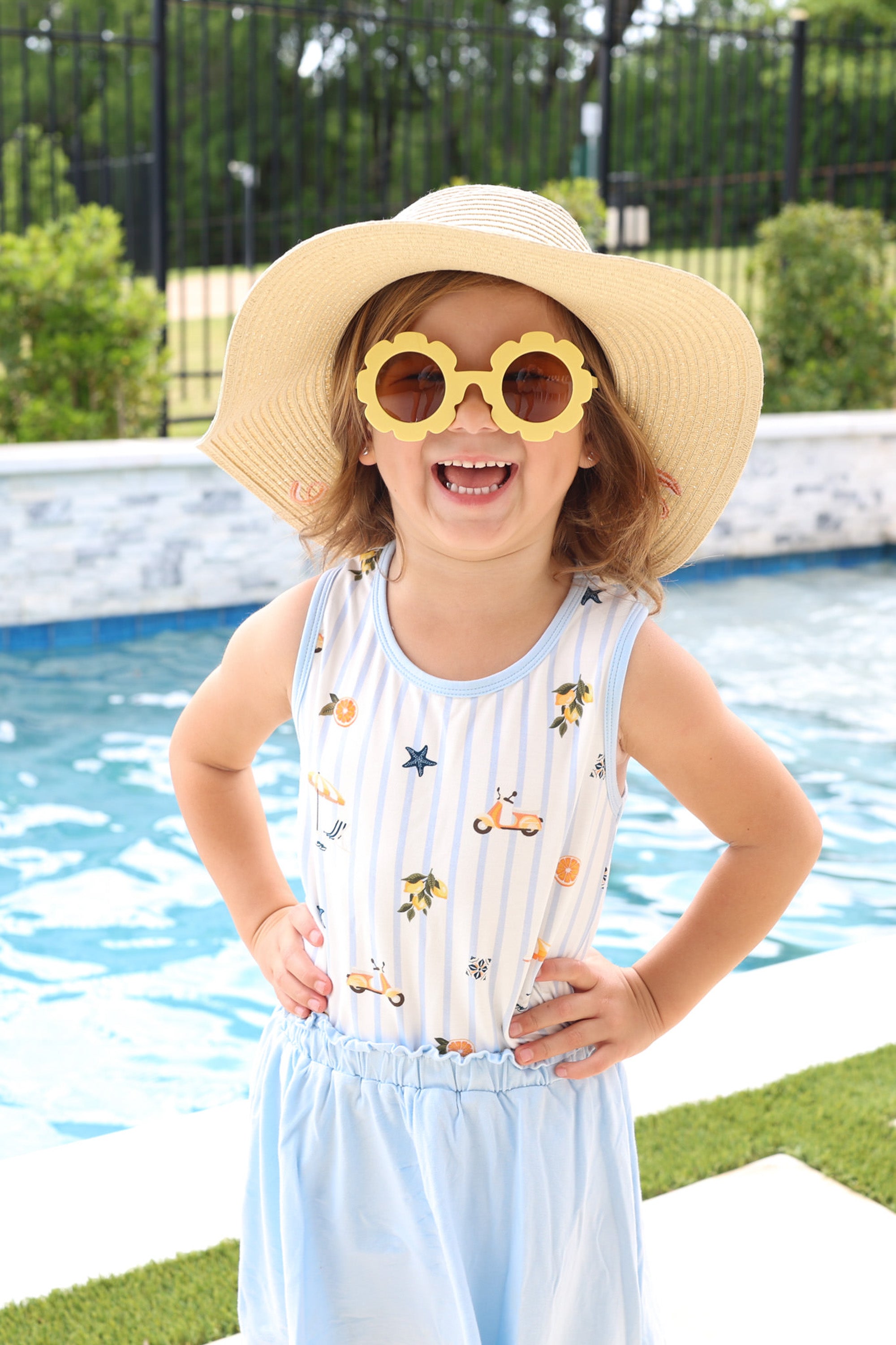 Smiling girl wearing a straw hat and yellow sunglasses wearing the Toddler Tank Top in Amalfi Coast with a light blue skort