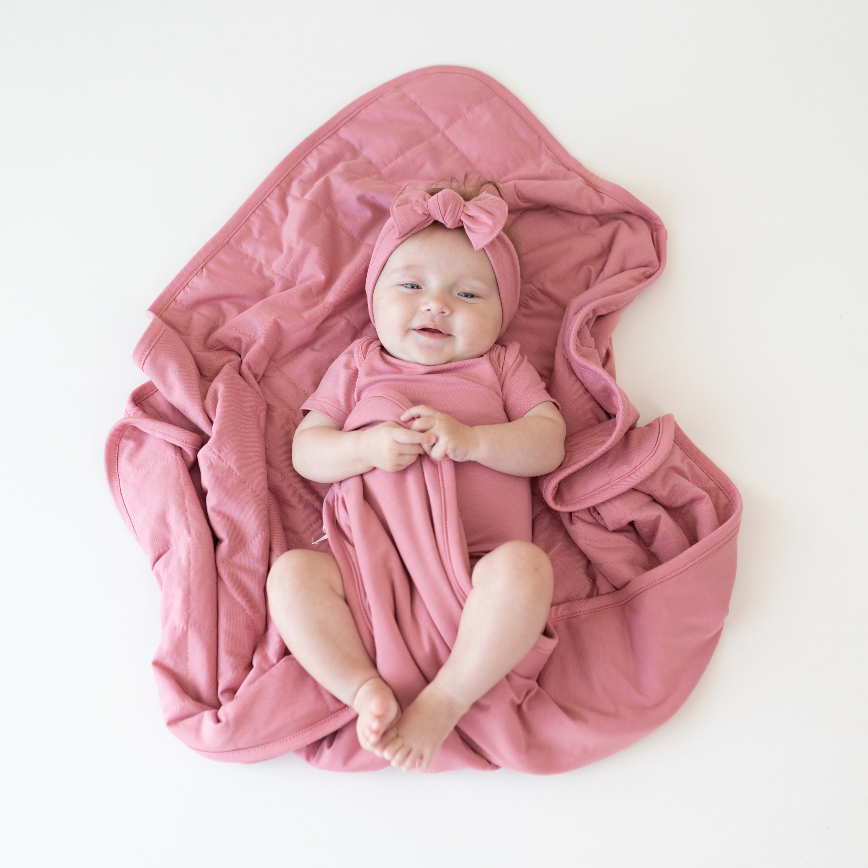 Baby wearing Apple Blossom Bodysuit and Bow laying on matching pink Baby Blanket