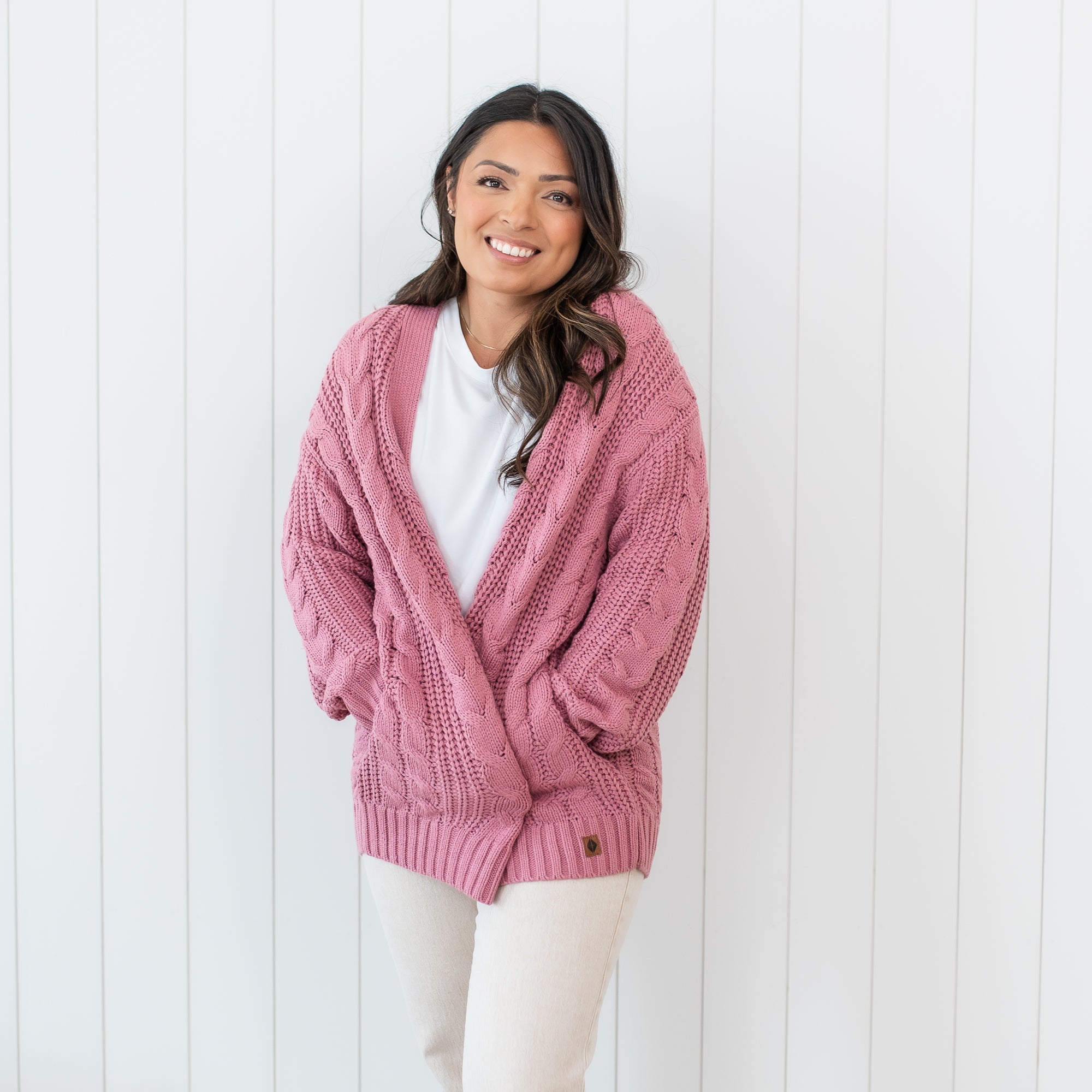 Smiling female standing with her hands in the pocket of the Cable Knit Adult Cardigan in Apple Blossom