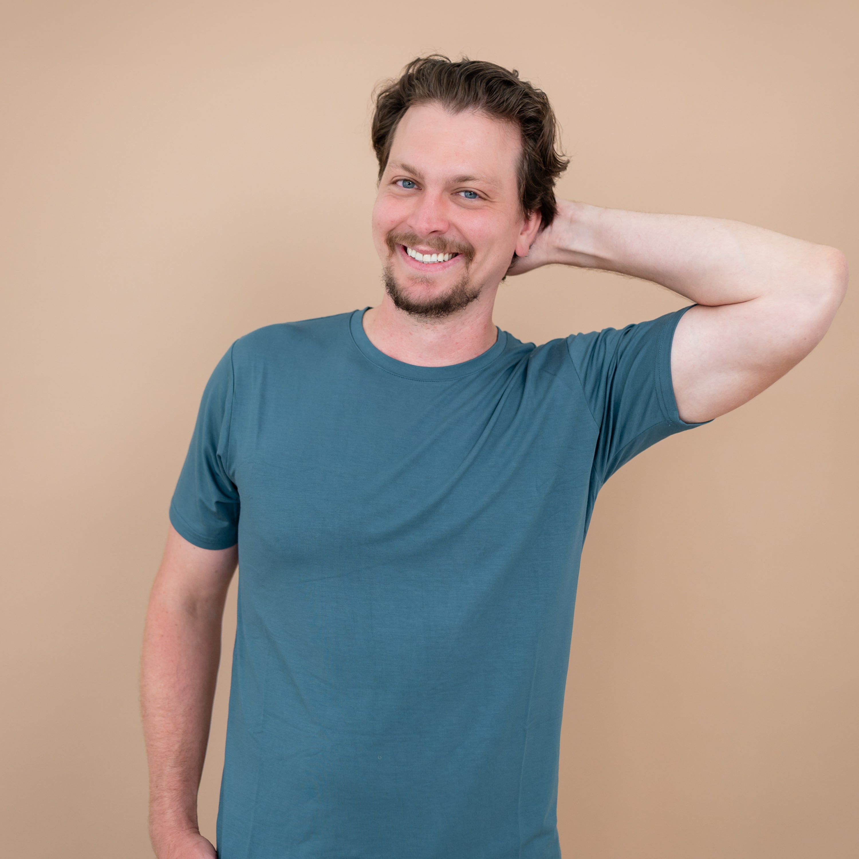 Smiling male model with one hand behind his head wearing the Men's Crew Neck Tee in Atlantic