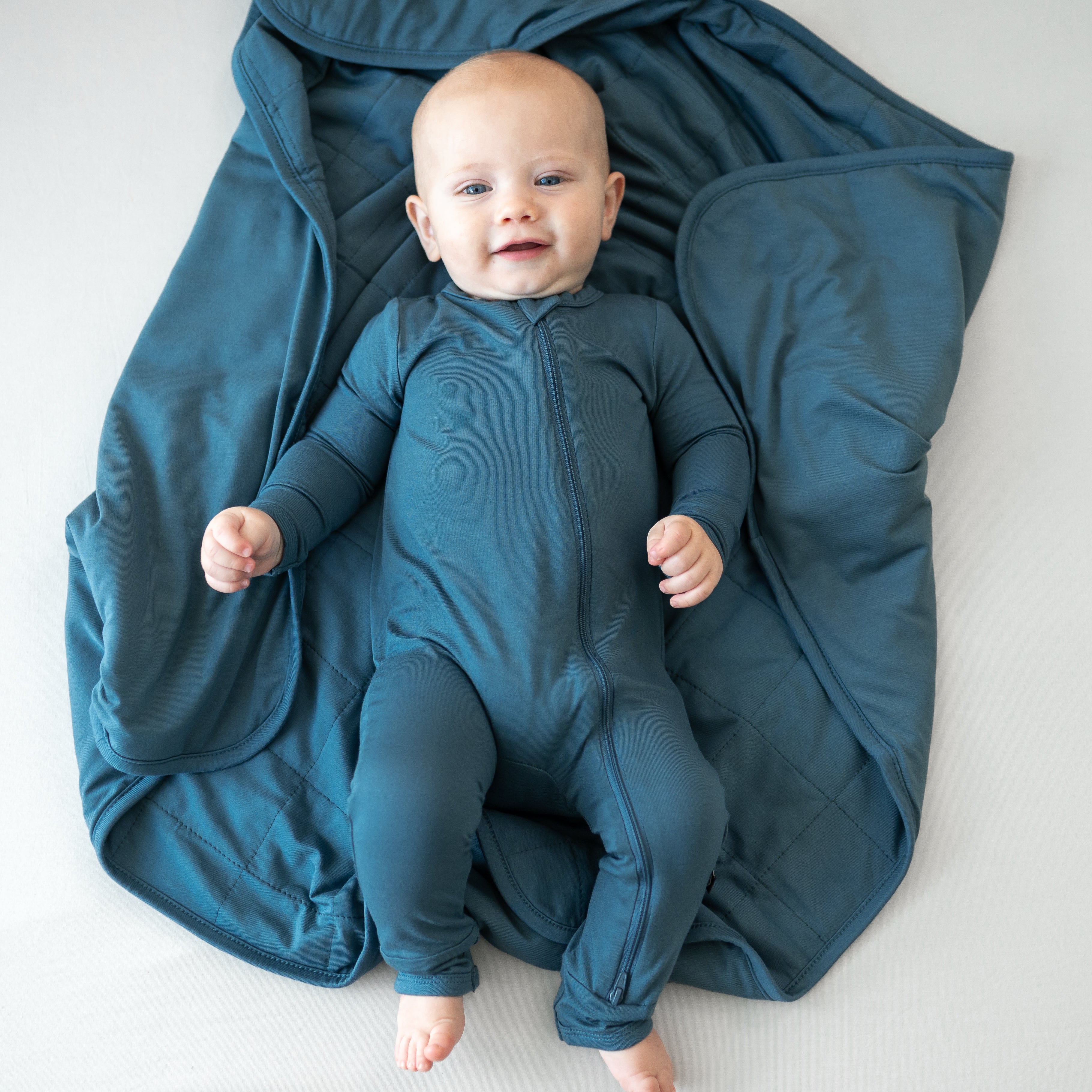 Infant laying on blue Baby Blanket in Atlantic TOG 1.0 wearing matching zippered romper pajamas