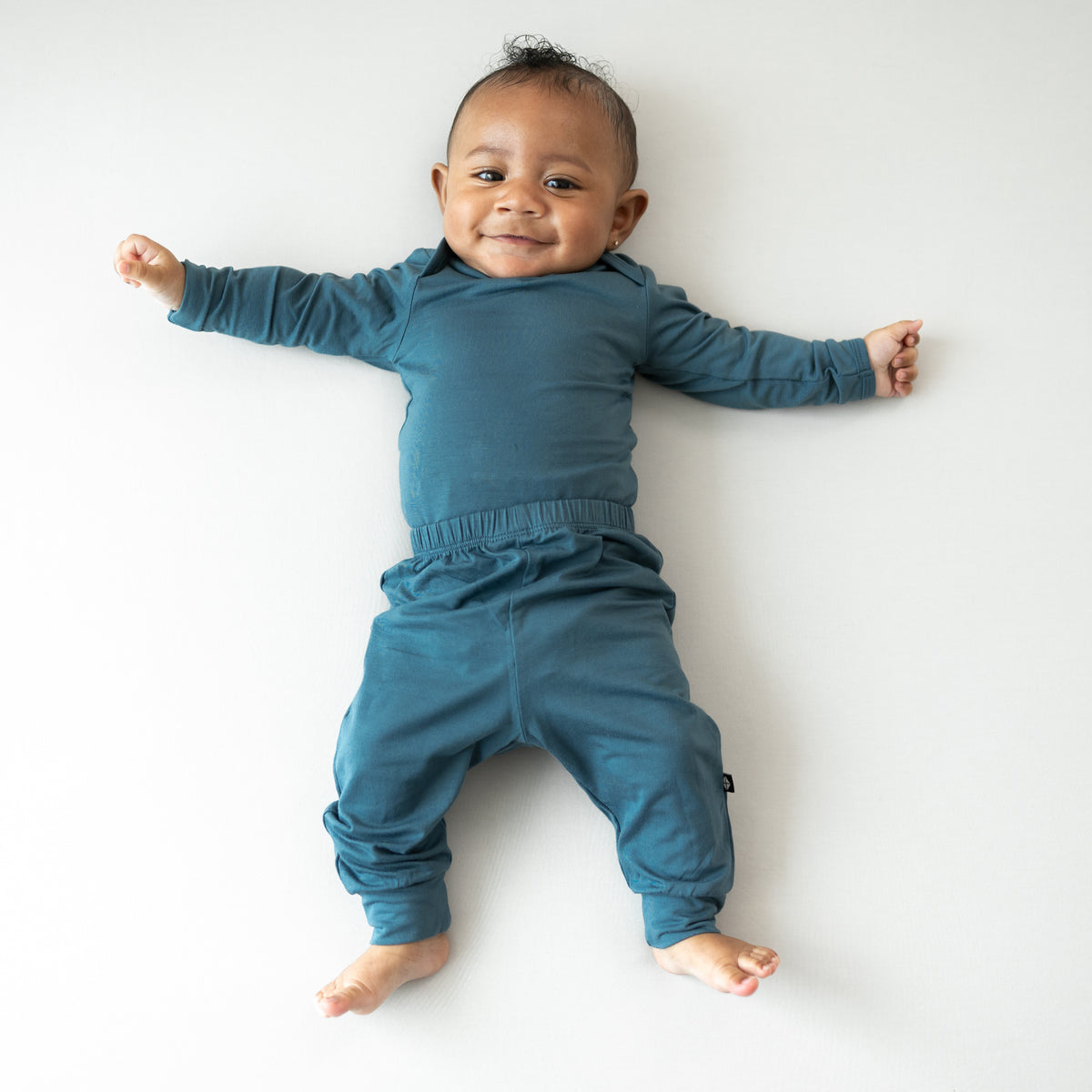 Smiling infant laying down wearing the Pant in Atlantic with matching long sleeve bodysuit