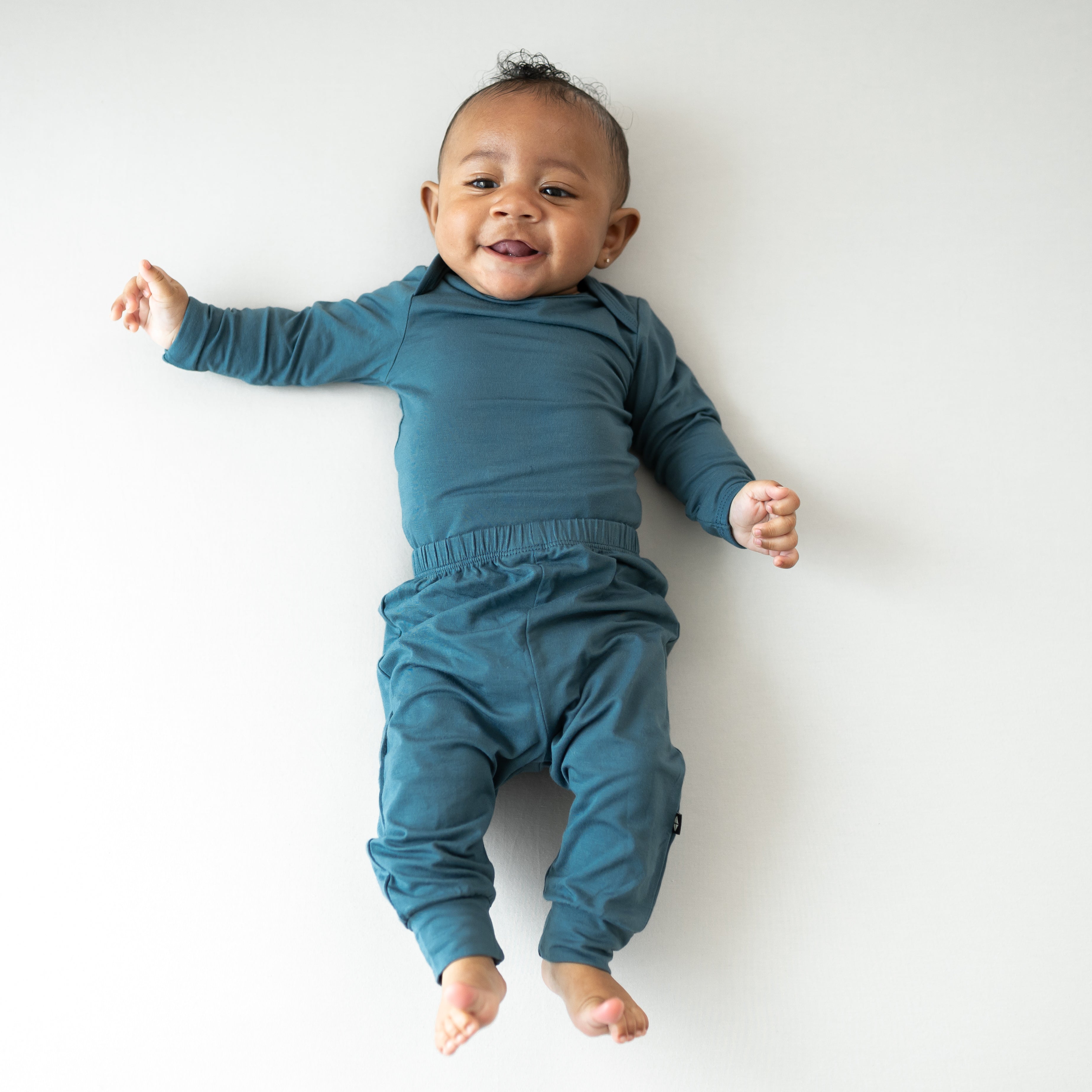 Infant laying down wearing the Long Sleeve Bodysuit in Atlantic paired with matching pants