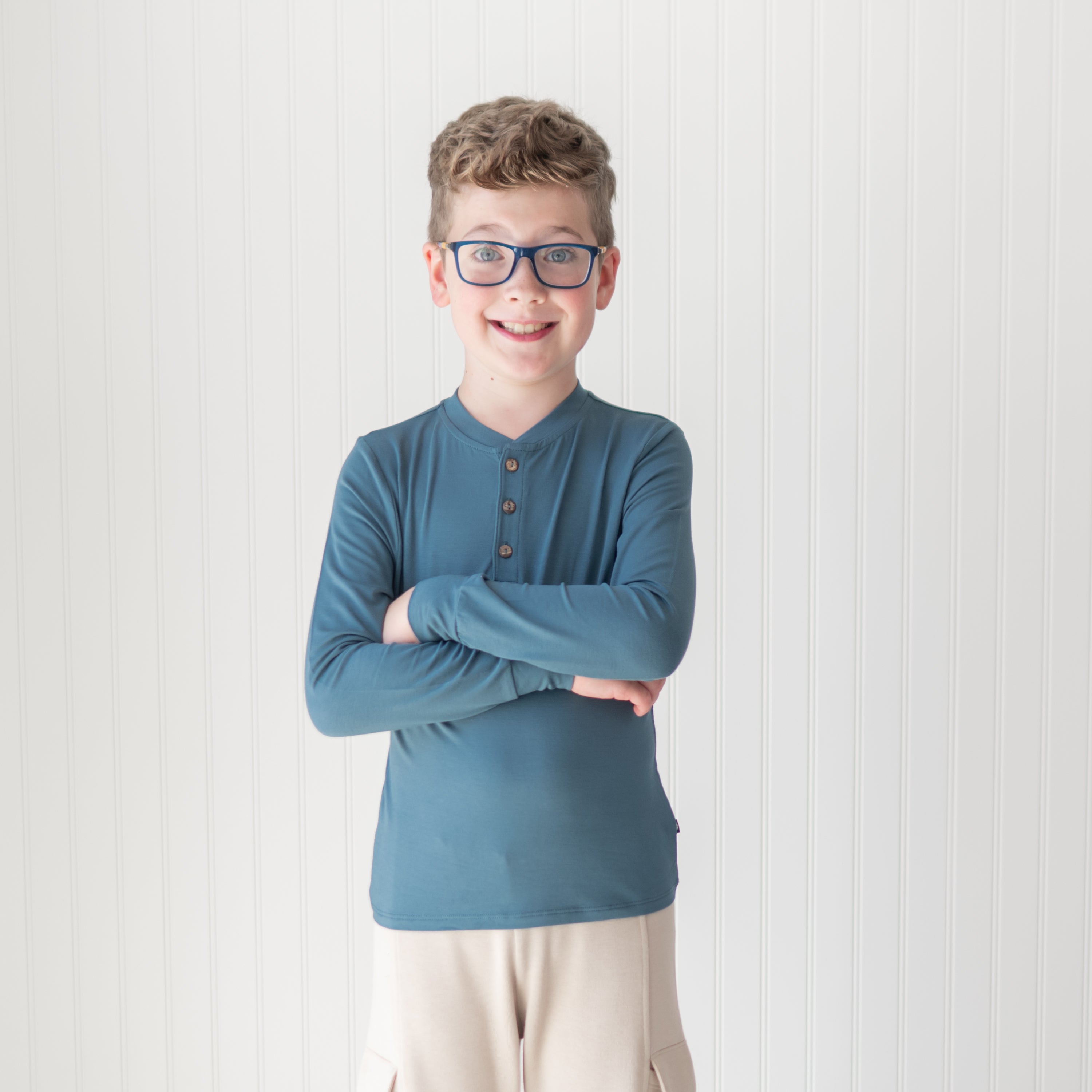 Young boy standing with his arms crossed in front of him wearing the Long Sleeve Toddler Henley Tee in Atlantic