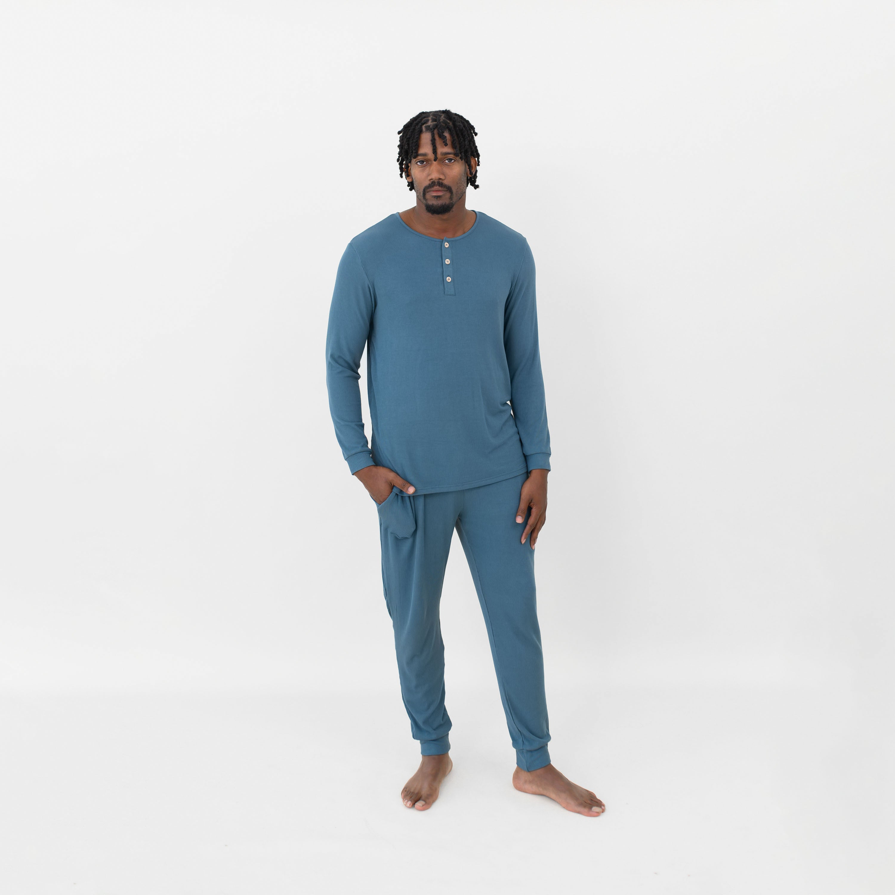 Male model standing wearing the Men's Ribbed Henley Set in Atlantic with one hand in the pants pocket in front of a white back drop