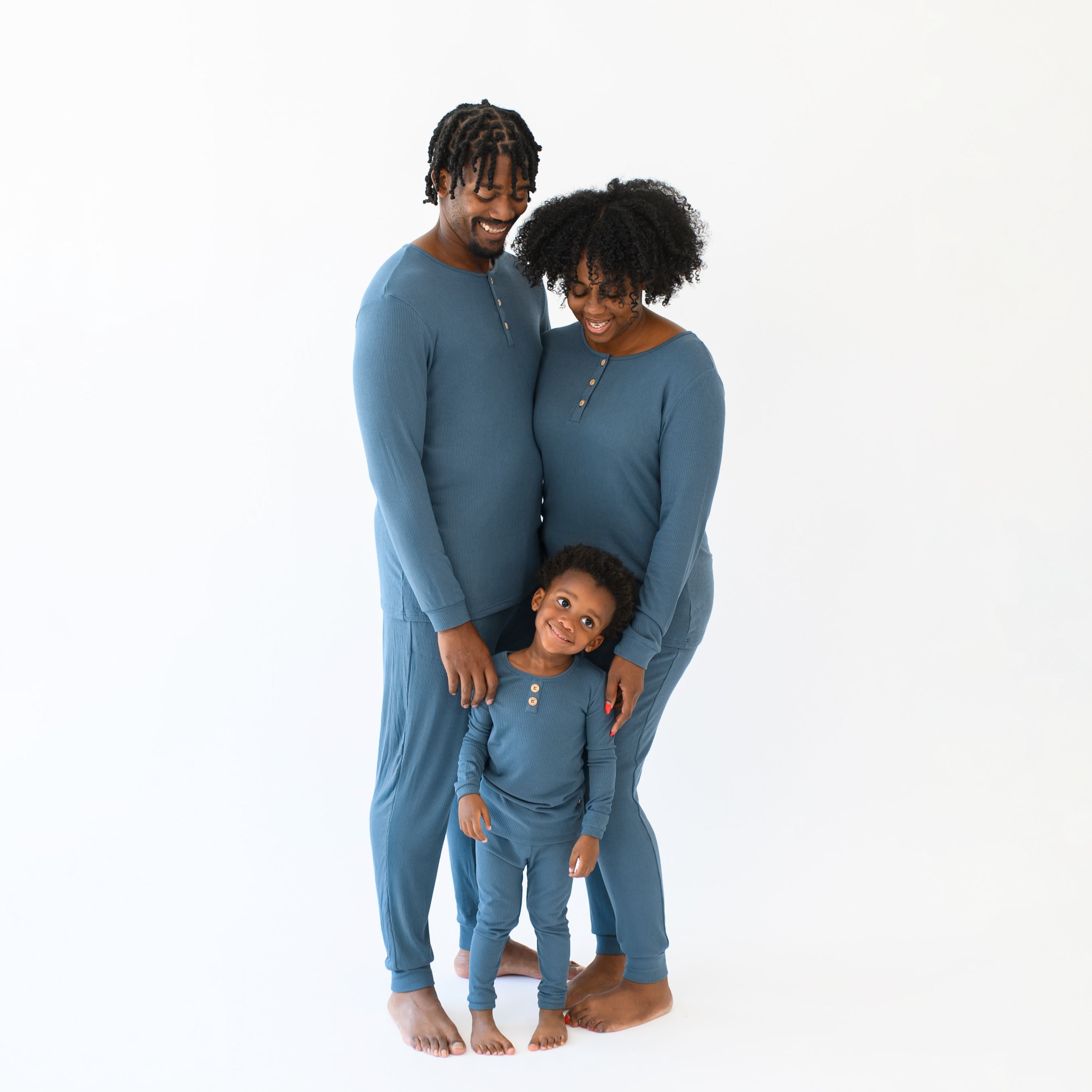 Family matching in Atlantic in front of a white background. Father standing beside his wife with their child in front of both of them, all are wearing the Ribbed Henley Sets in Atlantic