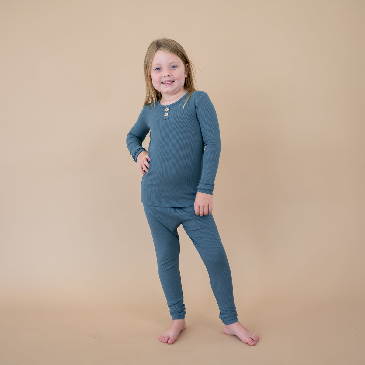 Young girl standing with one hand on her hip wearing the Ribbed Henley Set in Atlantic in front of a taupe colored background