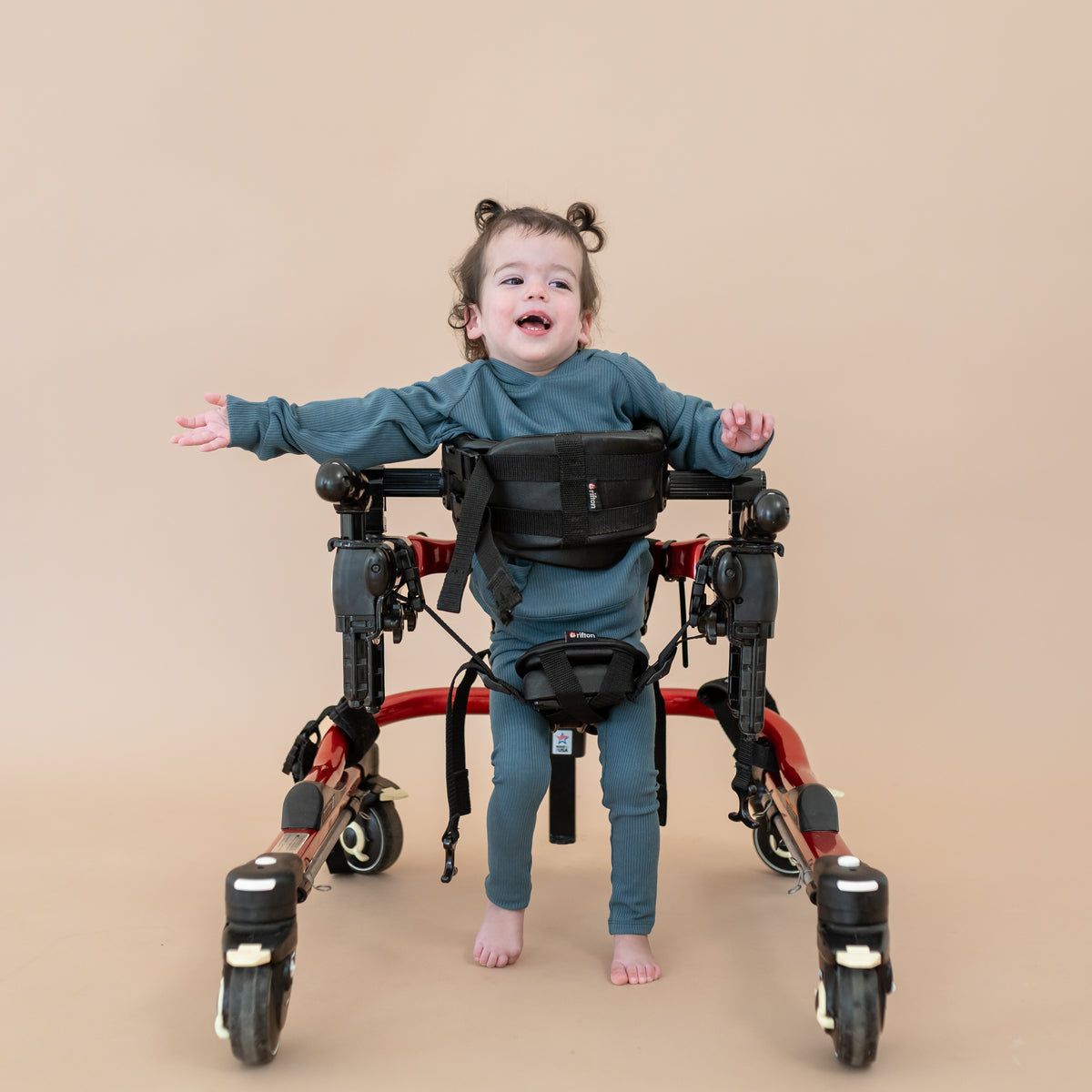 Smiling toddler wearing the Ribbed Hoodie in Atlantic and Ribbed Leggings in her walker in front of a taupe background