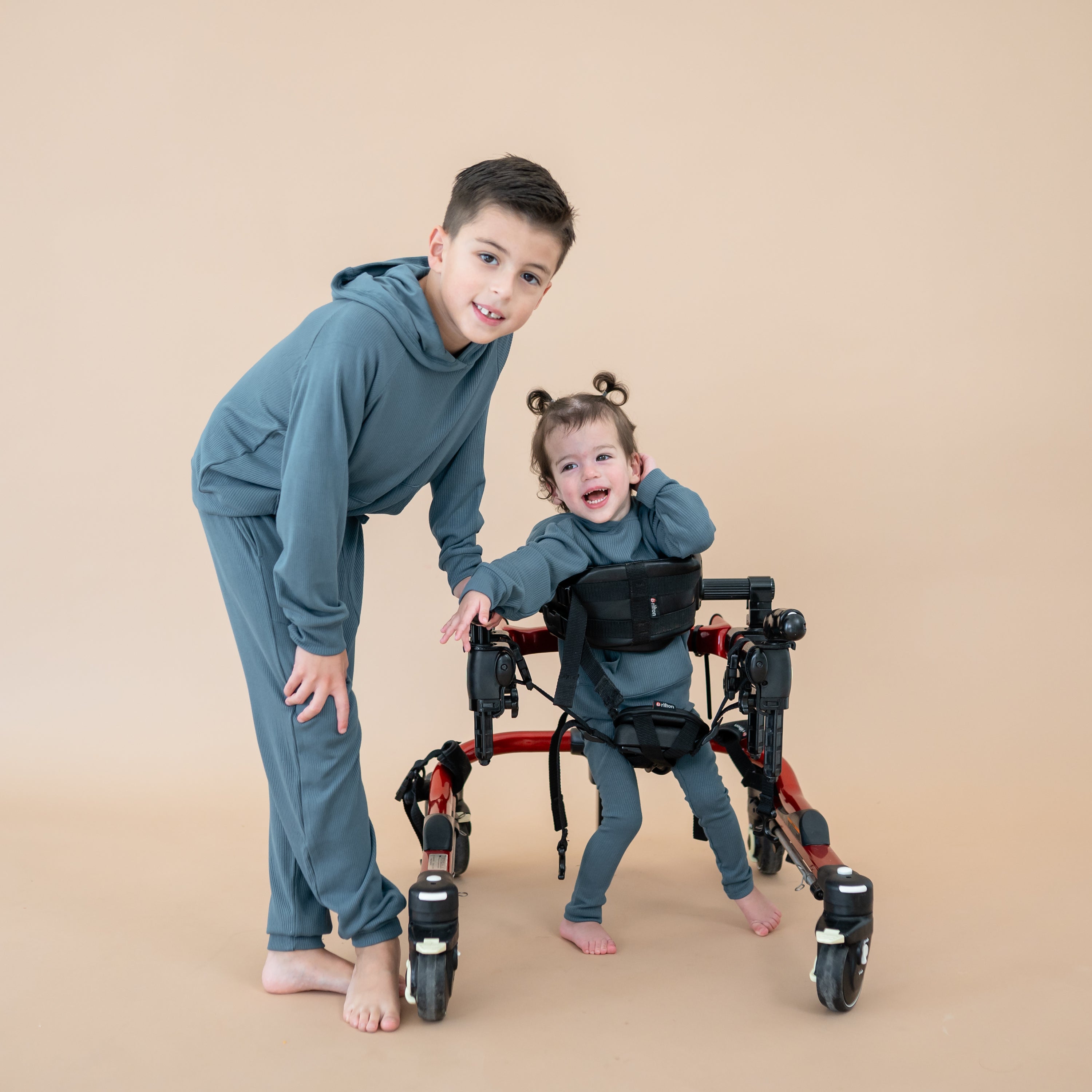 Smiling brother wearing the Ribbed Hoodie in Atlantic and Ribbed Jogger pants standing beside sister wearing the Ribbed Leggings in Atlantic and matching ribbed hoodie