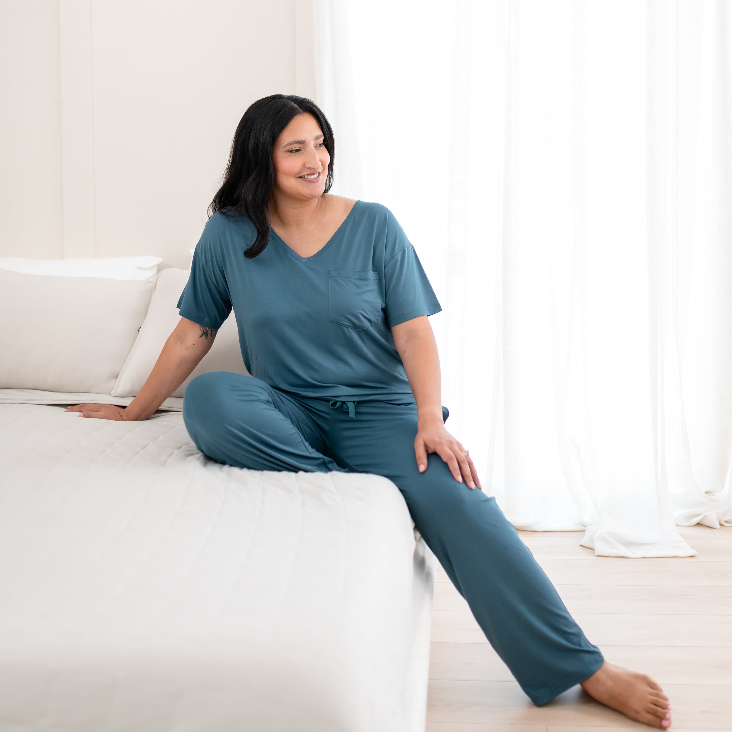 Female model sitting on a bed wearing the Women’s Relaxed Fit V-Neck in Atlantic with matching women's lounge pants