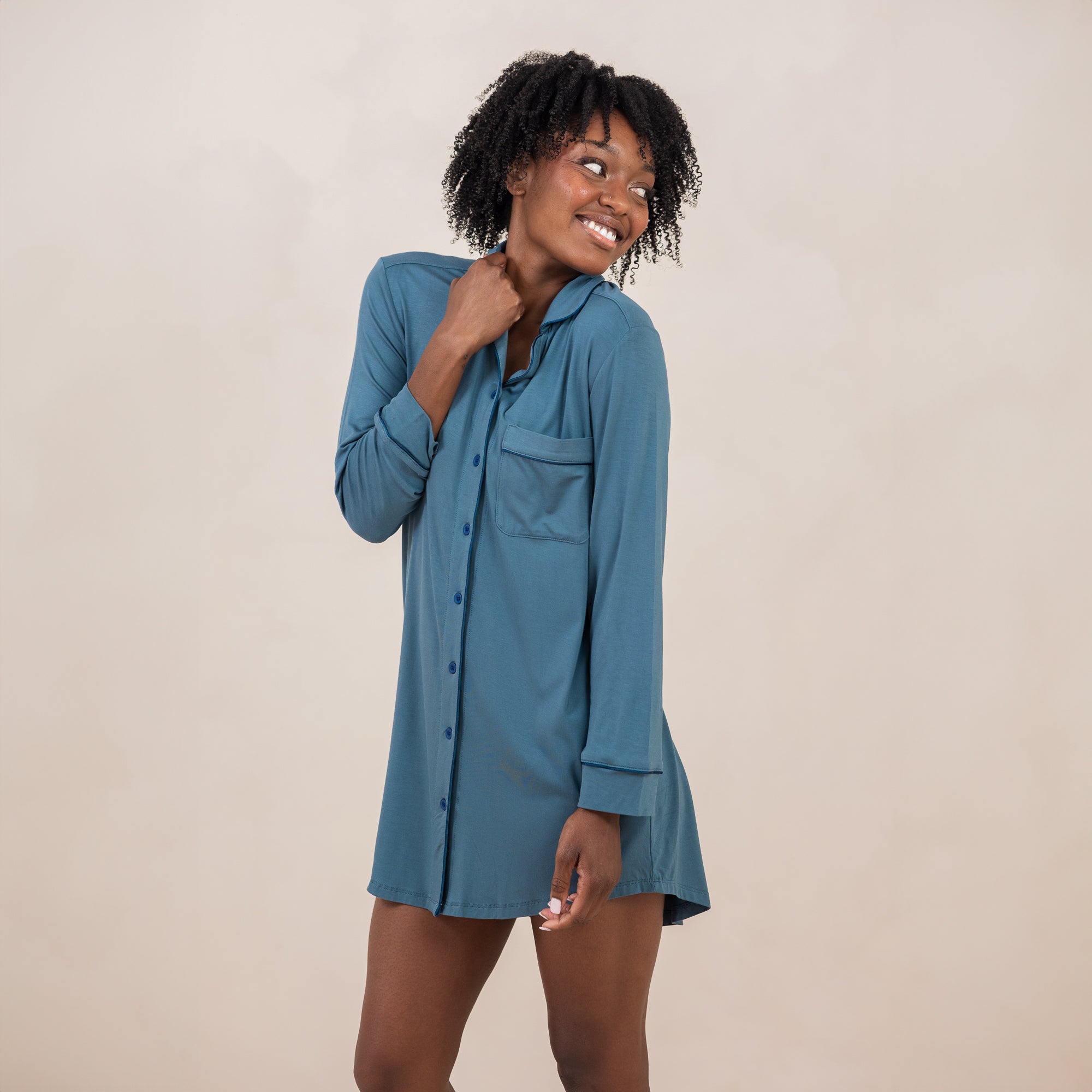 Smiling female model wearing the with one hand on the collar of the shirt and the other hand down at her side