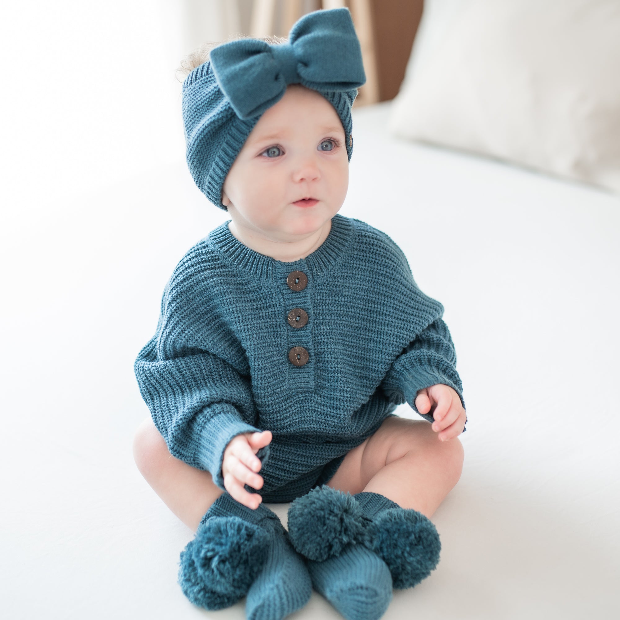Toddler sitting wearing the Chunky Knit Romper in Atlantic and matching chunky knit bow headband and knit booties