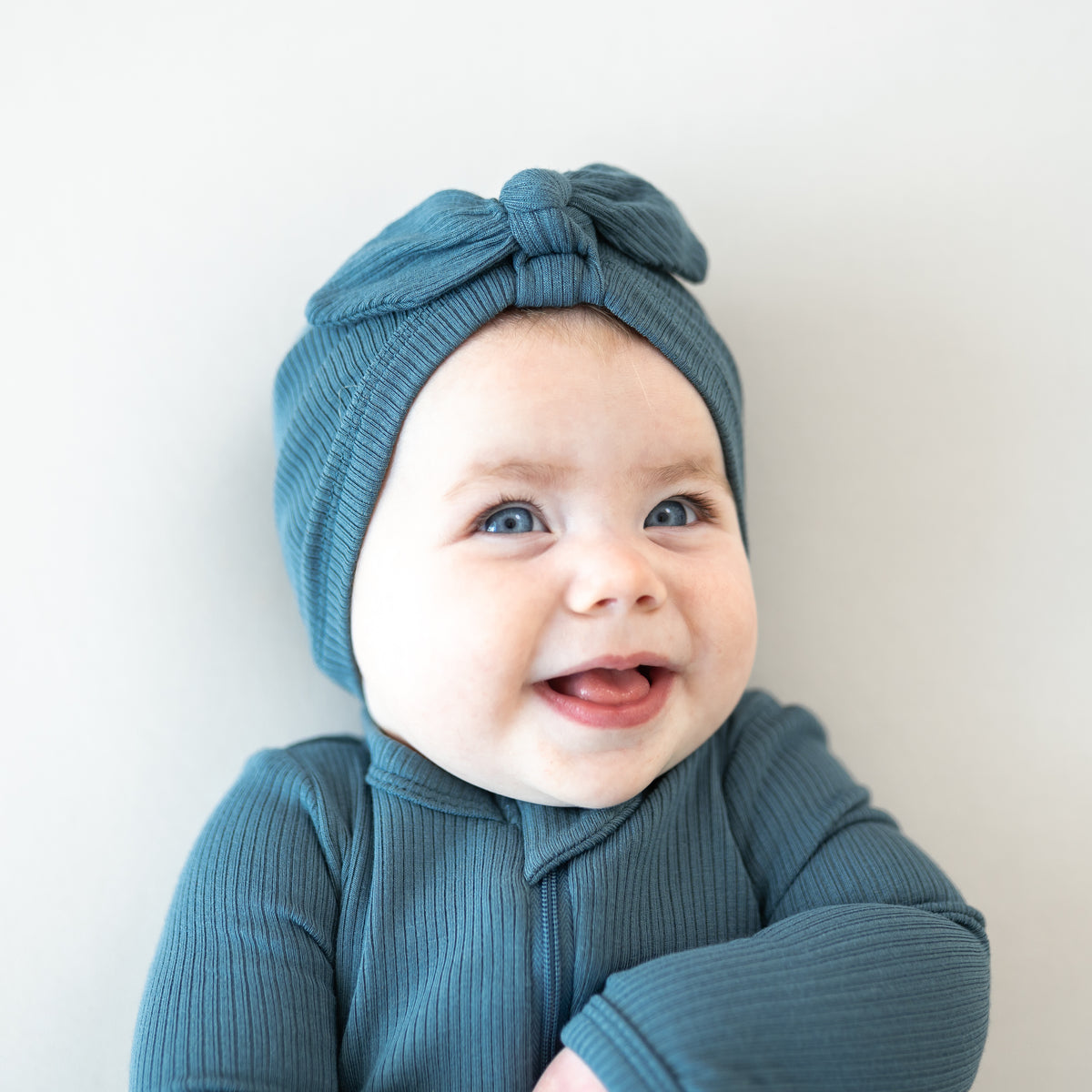 Close up of infant girl wearing the Ribbed Headwrap in Atlantic on a light colored background