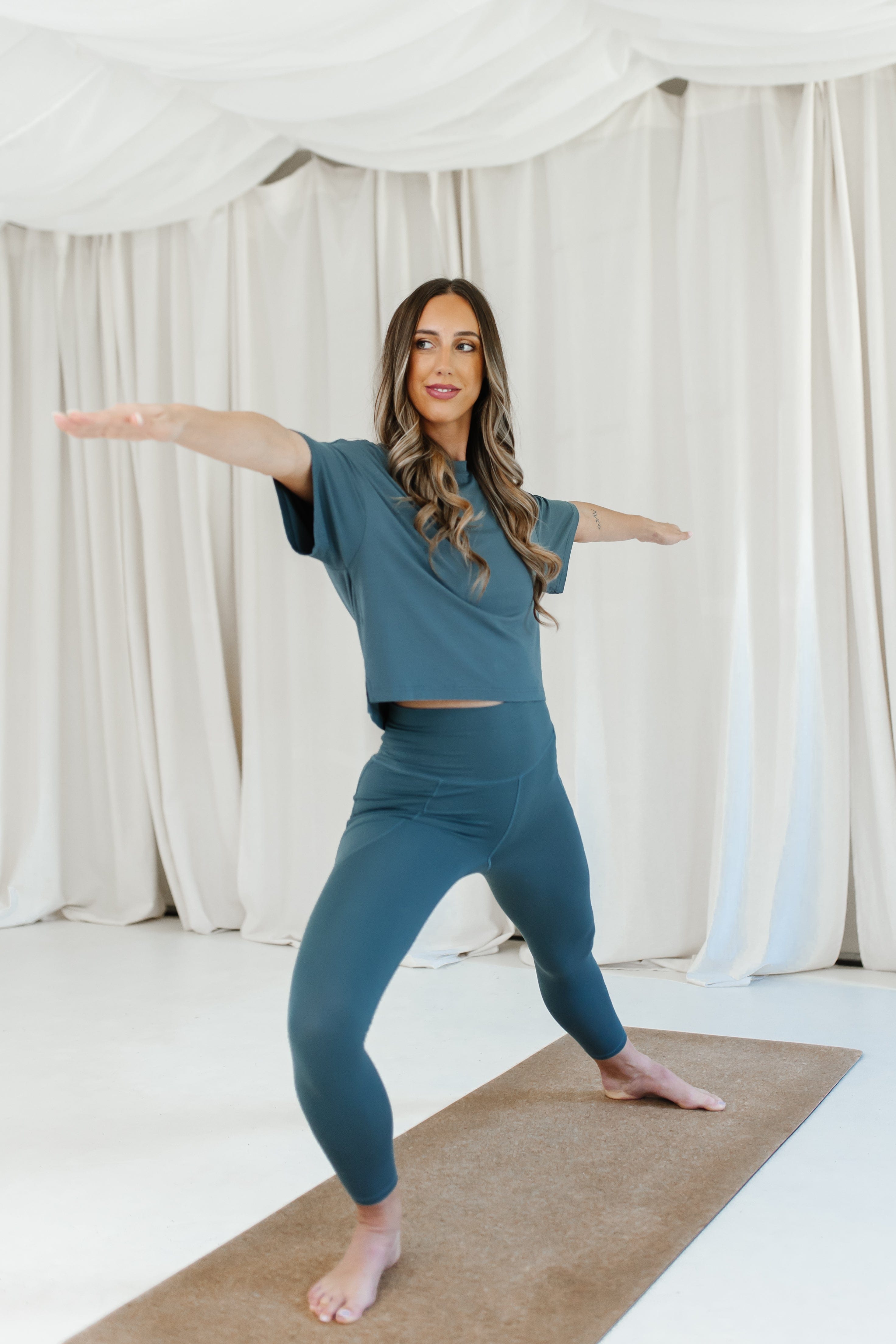 Female model wearing the Bamboo Flex Women’s Leggings in Atlantic and matching short sleeve tee doing a yoga pose