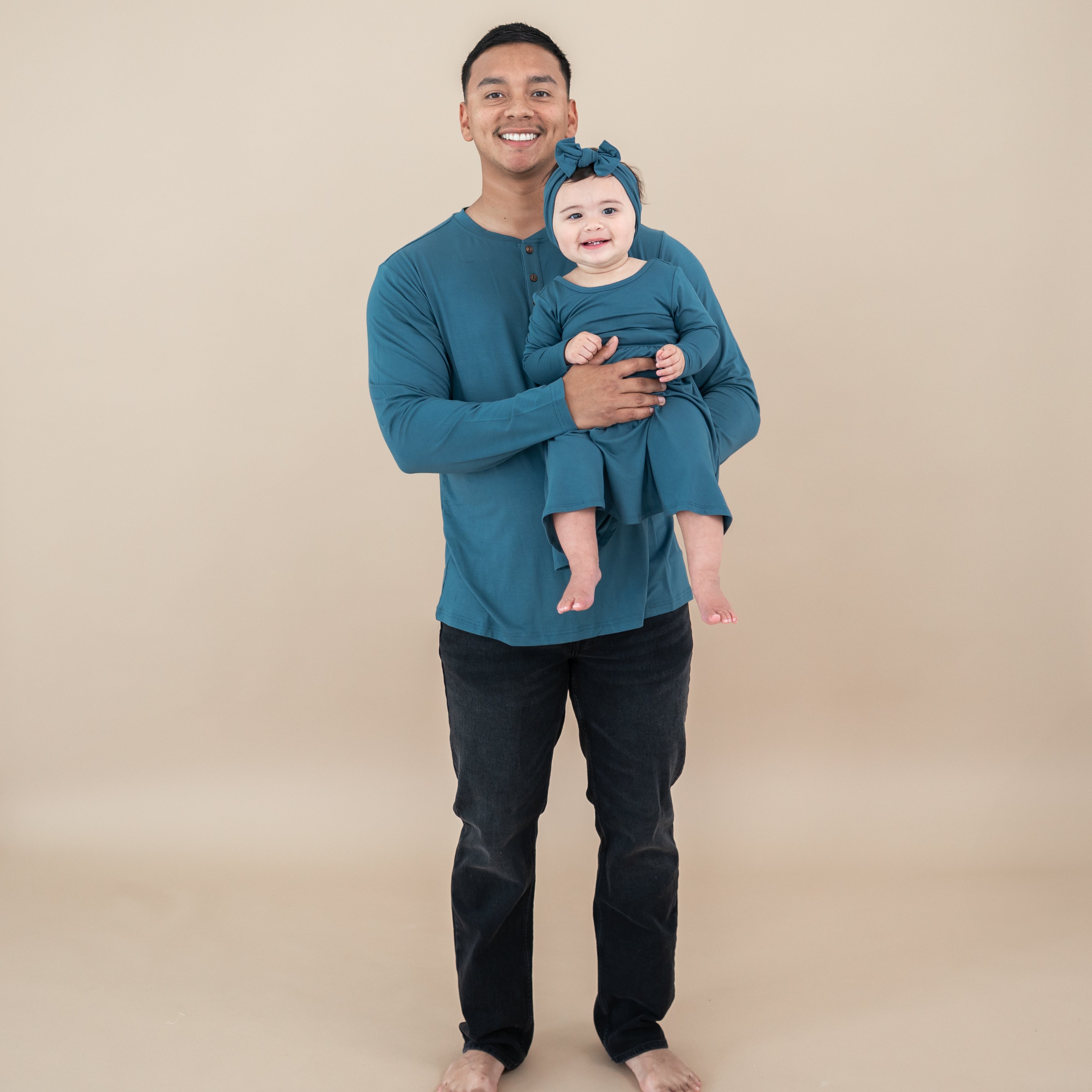 Father and daughter matching in Atlantic. Daughter is wearing a Long Sleeve twirl dress being held by her father who is wearing the Men's Long Sleeve Henley Top