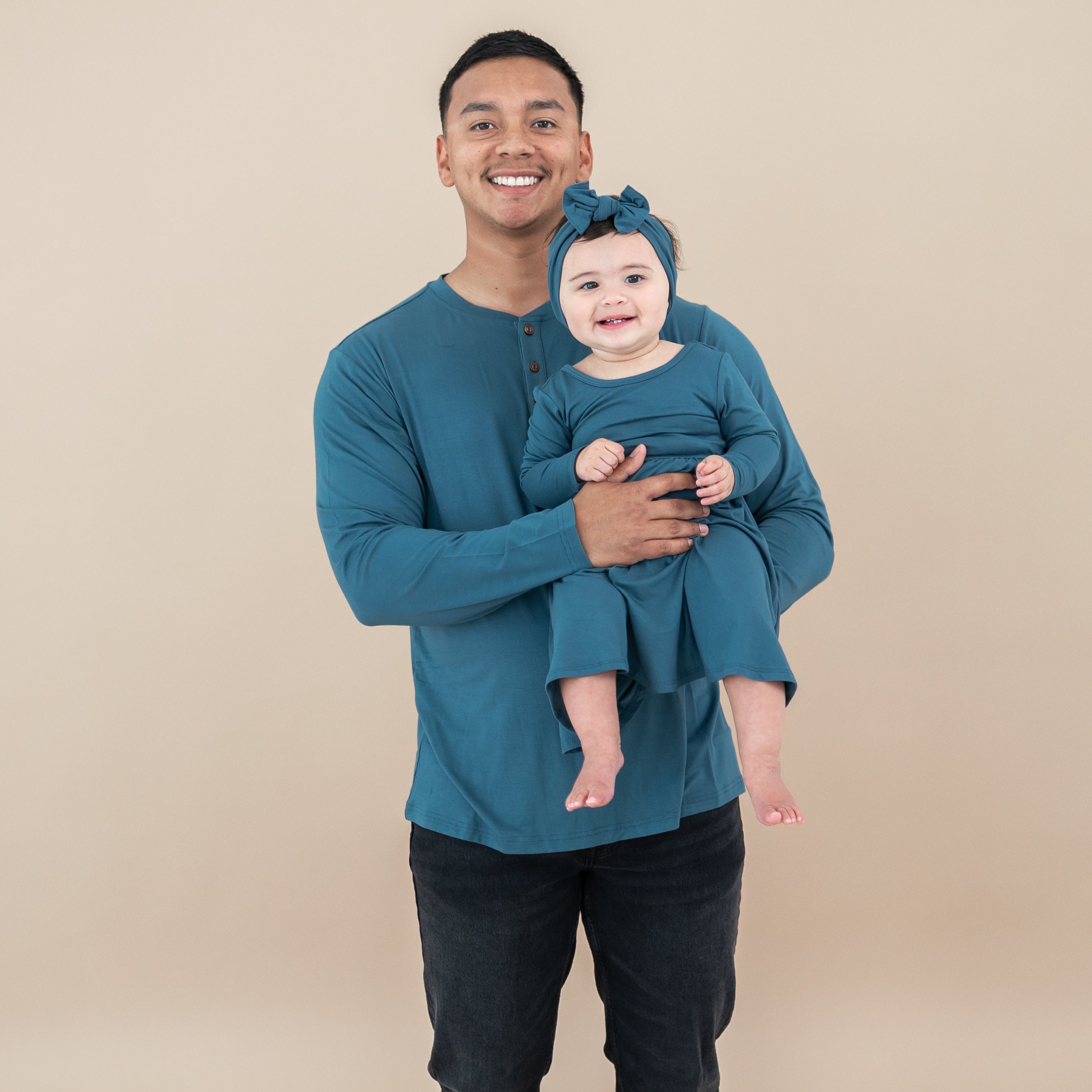 Father and daughter matching in Atlantic. Daughter is wearing a Long Sleeve twirl dress being held by her father who is wearing the Men's Long Sleeve Henley Top